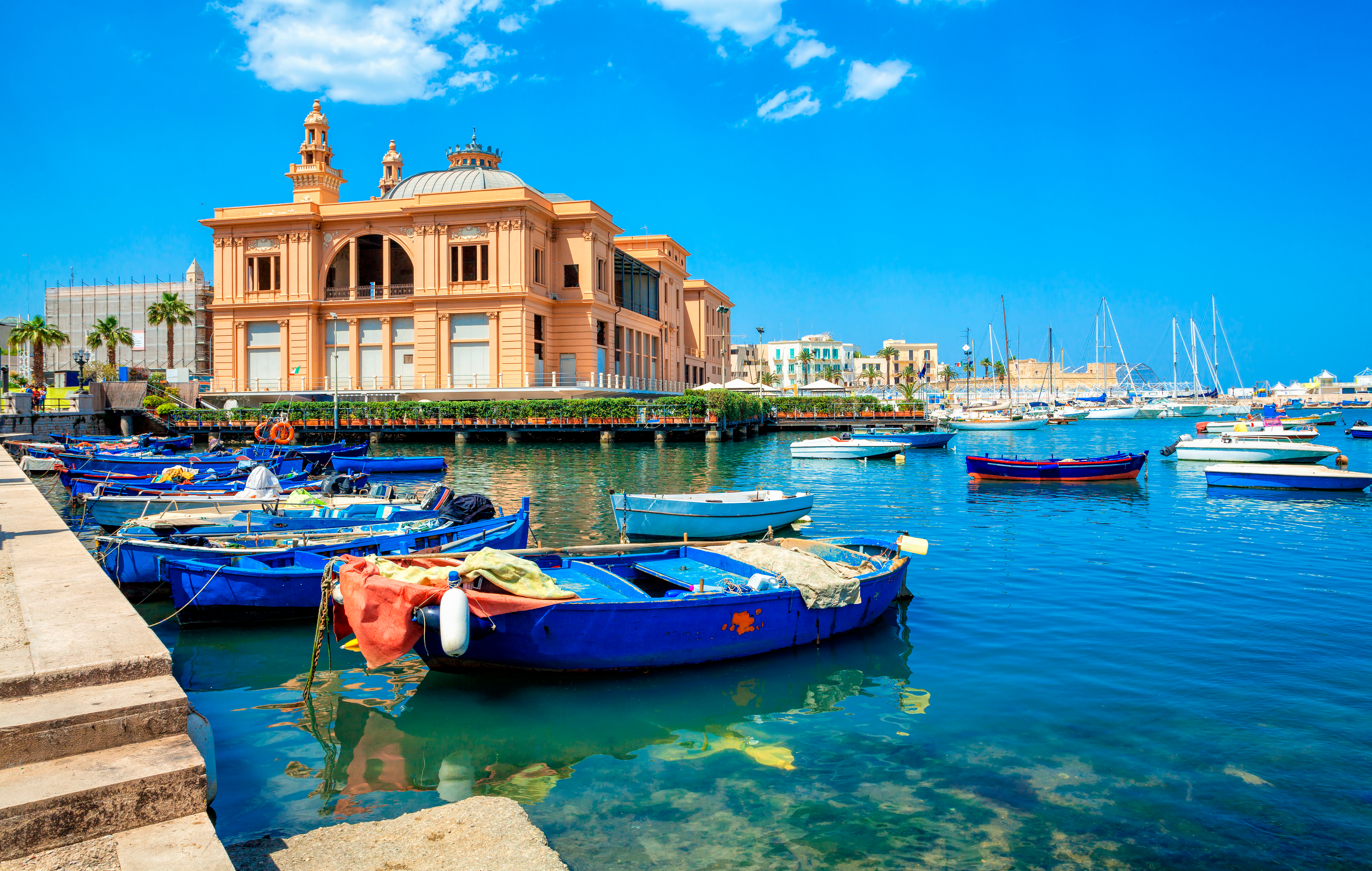 Stemningsfuld havn i Bari, Puglia, med blå træbåde fortøjet foran det pragtfulde Teatro Margherita ved Middelhavet
