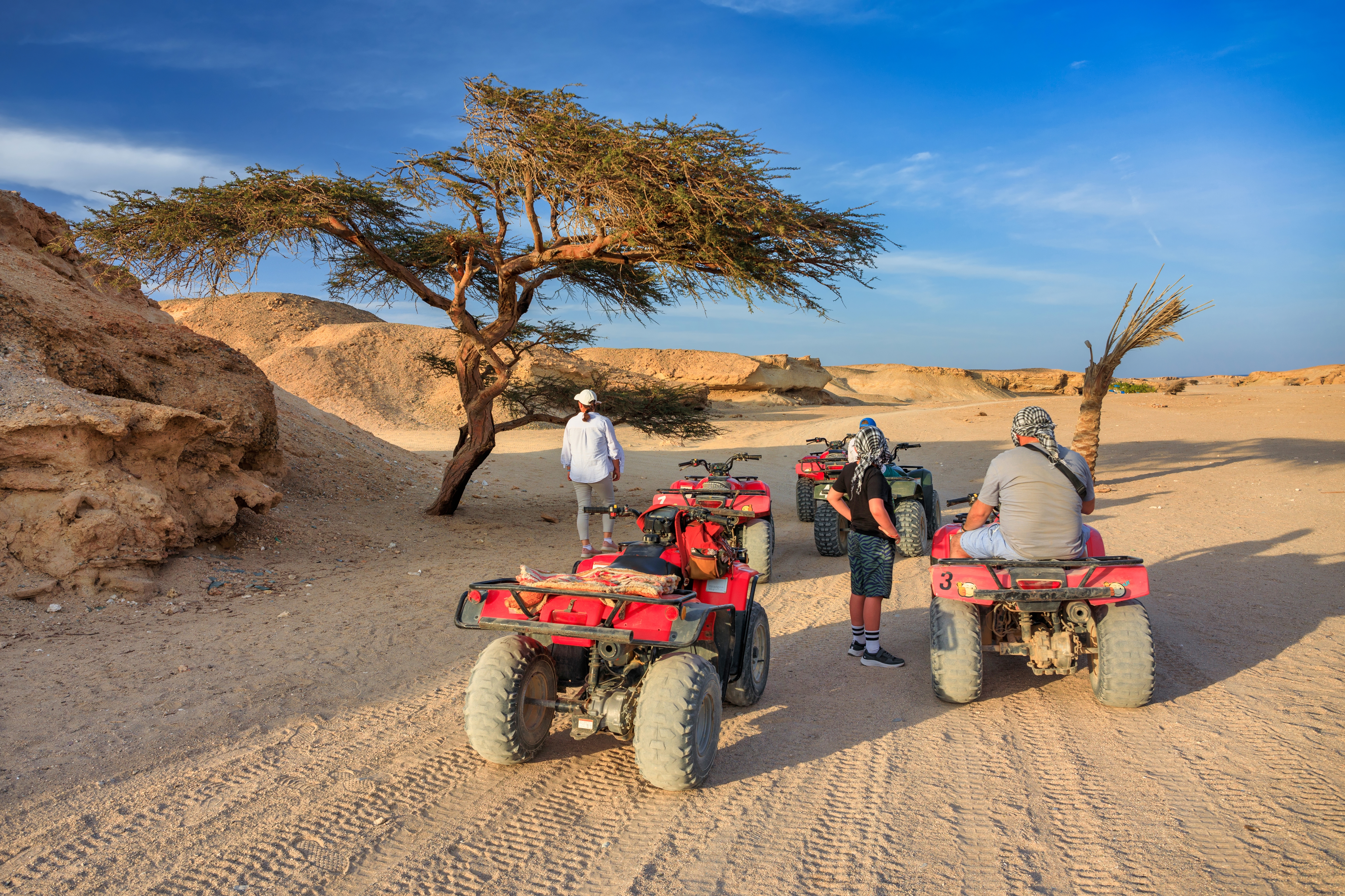 Turister på røde quad bikes i den egyptiske ørken nær Marsa Alam med sandklitter og blå himmel