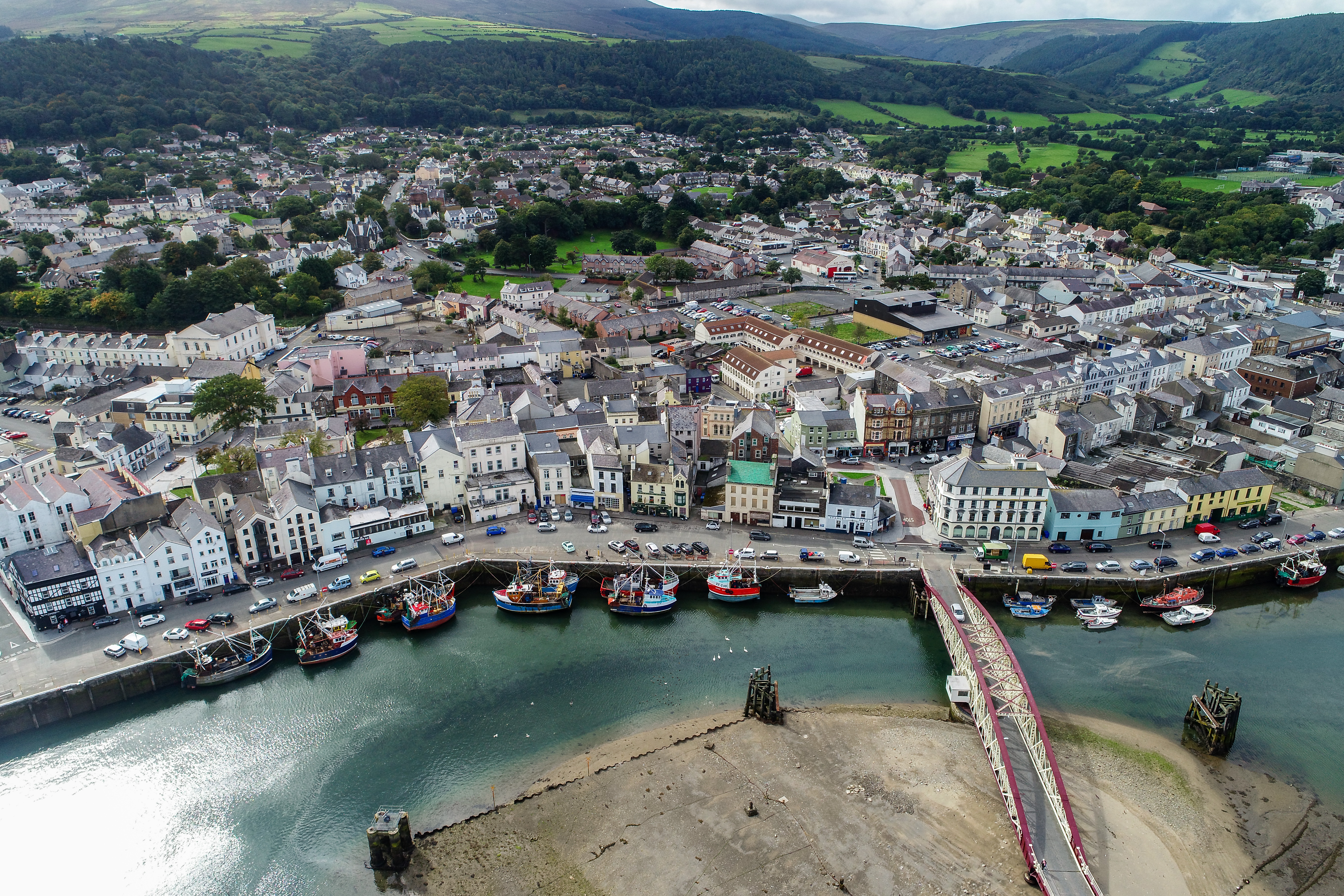 Drone-foto af Ramsey havn og bymidte på Isle of Man med farverige bygninger, fiskerbåde og grønne bjerge i baggrunden