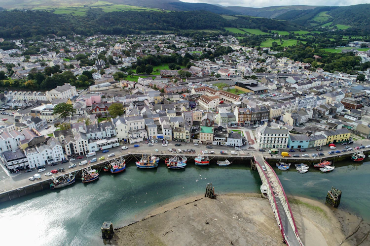 Drone-foto af Ramsey havn og bymidte på Isle of Man med farverige bygninger, fiskerbåde og grønne bjerge i baggrunden