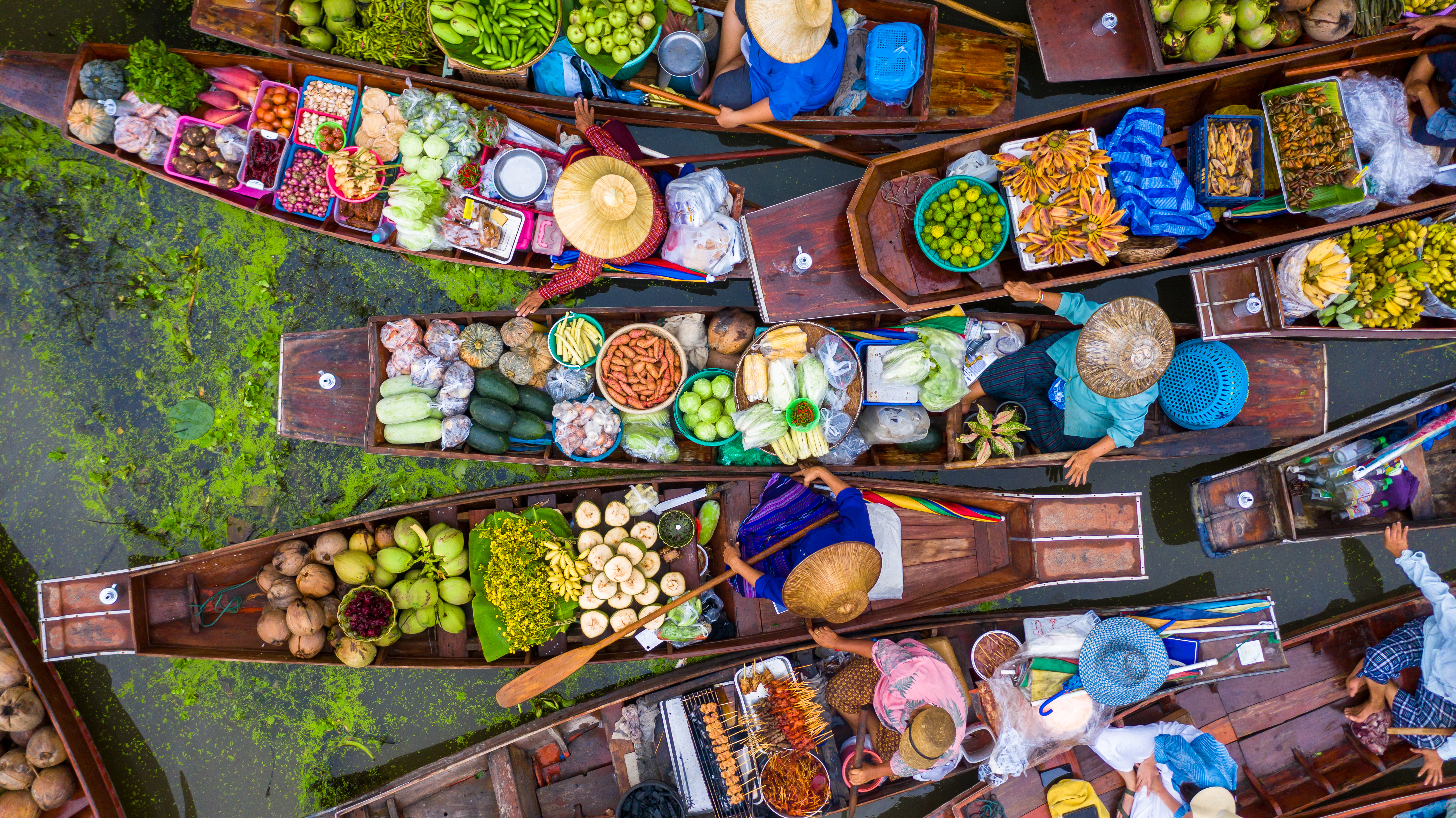Malerisk luftfoto af det ikoniske Damnoen Saduak flydende marked i Thailand, hvor lokale handlende sælger friske råvarer og thailandske specialiteter fra farverige træbåde