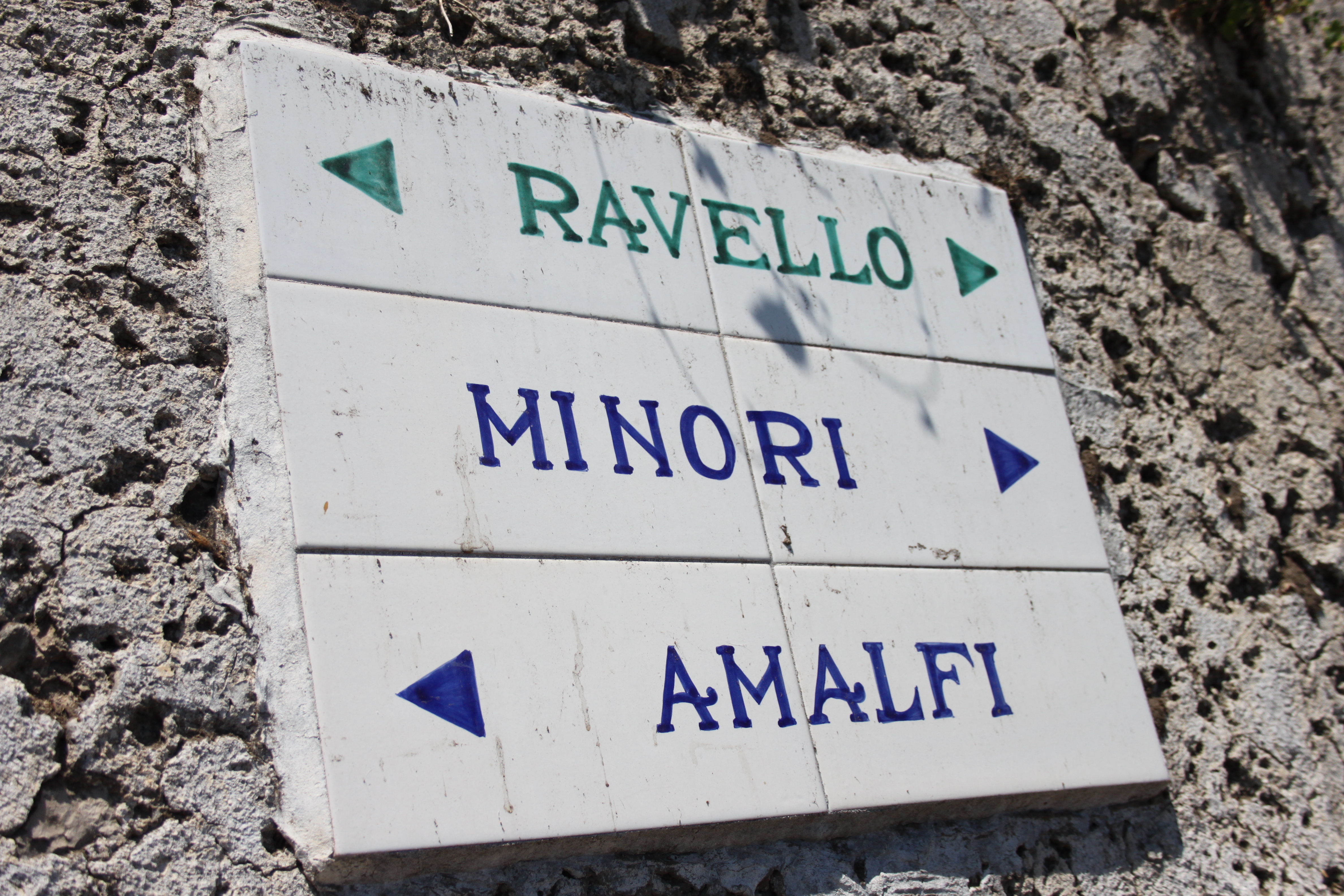 Hvidt fliseskilt med pile der viser retning til Ravello, Minori og Amalfi på den italienske Amalfikysten
