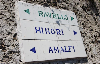Hvidt fliseskilt med pile der viser retning til Ravello, Minori og Amalfi på den italienske Amalfikysten