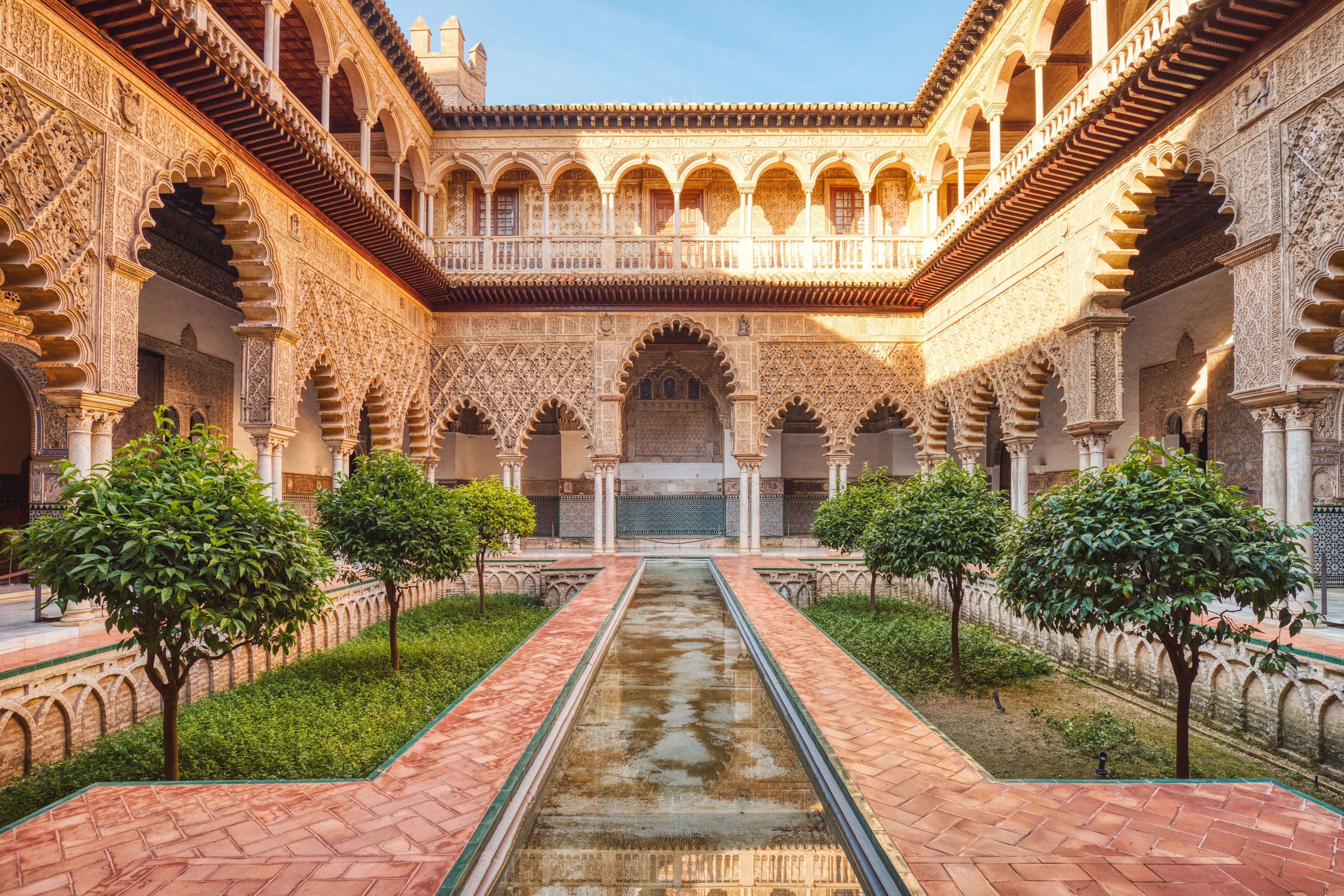 Elegant gårdhave i det historiske Real Alcazar i Sevilla med slanke søjler, dekorative buer og detaljerede arabiske ornamenter - oplev det kongelige palads' unikke blanding af islamisk og spansk arkitektur i Andalusien