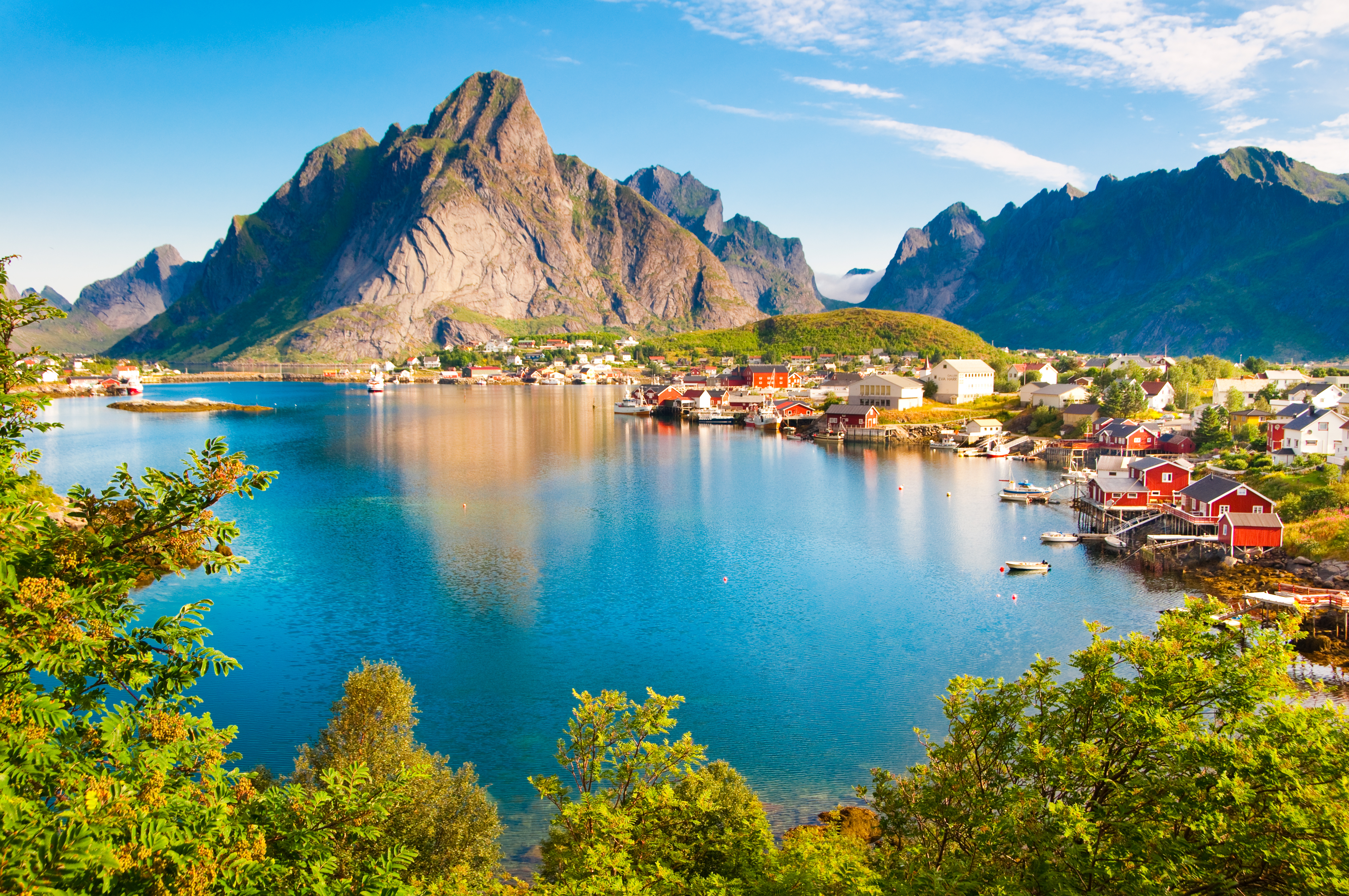 Spektakulær panoramaudsigt over den lille fiskerby Reine med dens karakteristiske røde rorbuer ved foden af de mægtige bjerge og det krystalklare fjordvand på Lofoten