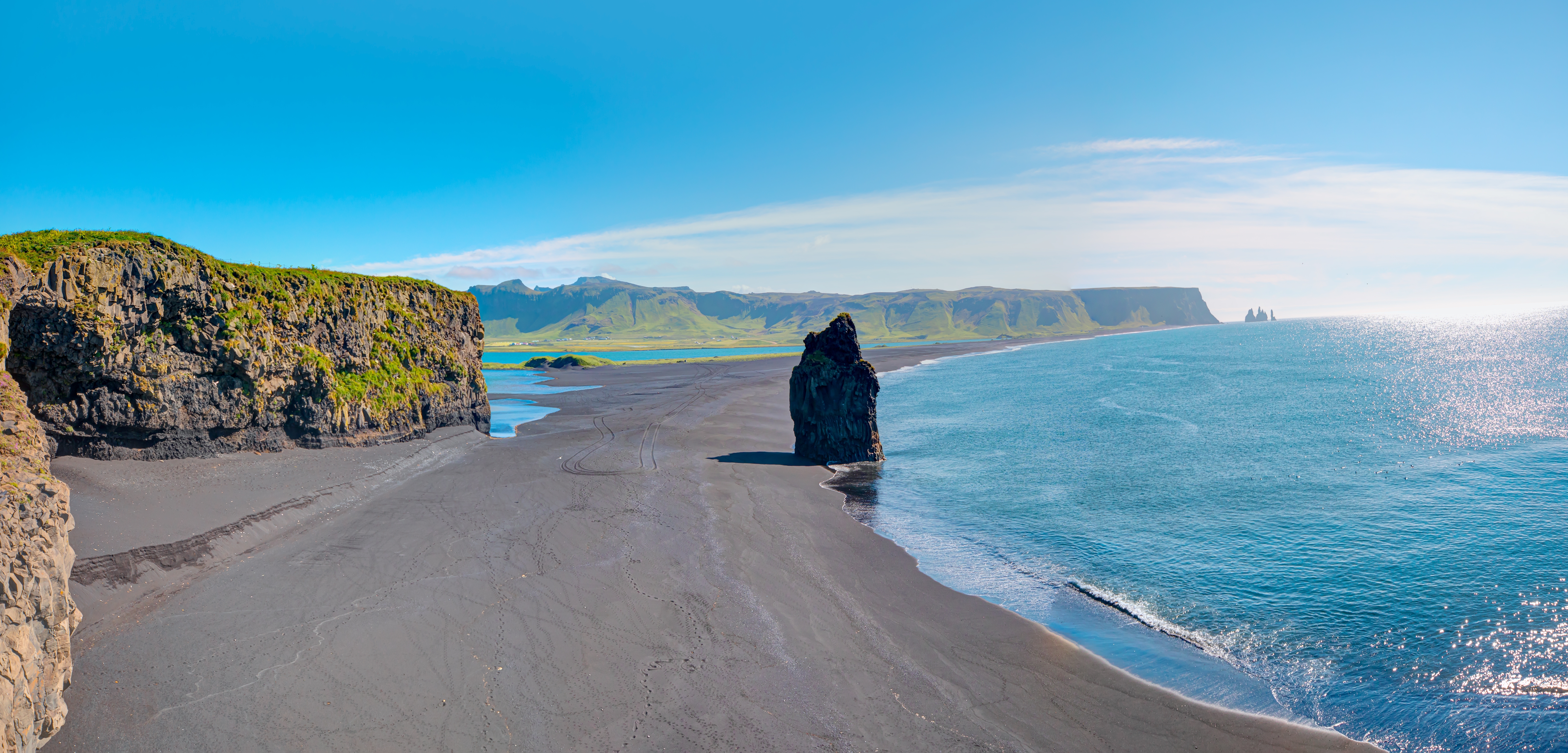 Den smukke sorte sandstrand Reynisfjara på Island nær Vik med dramatiske basaltformationer, turkist hav og grønne klippeskrænter