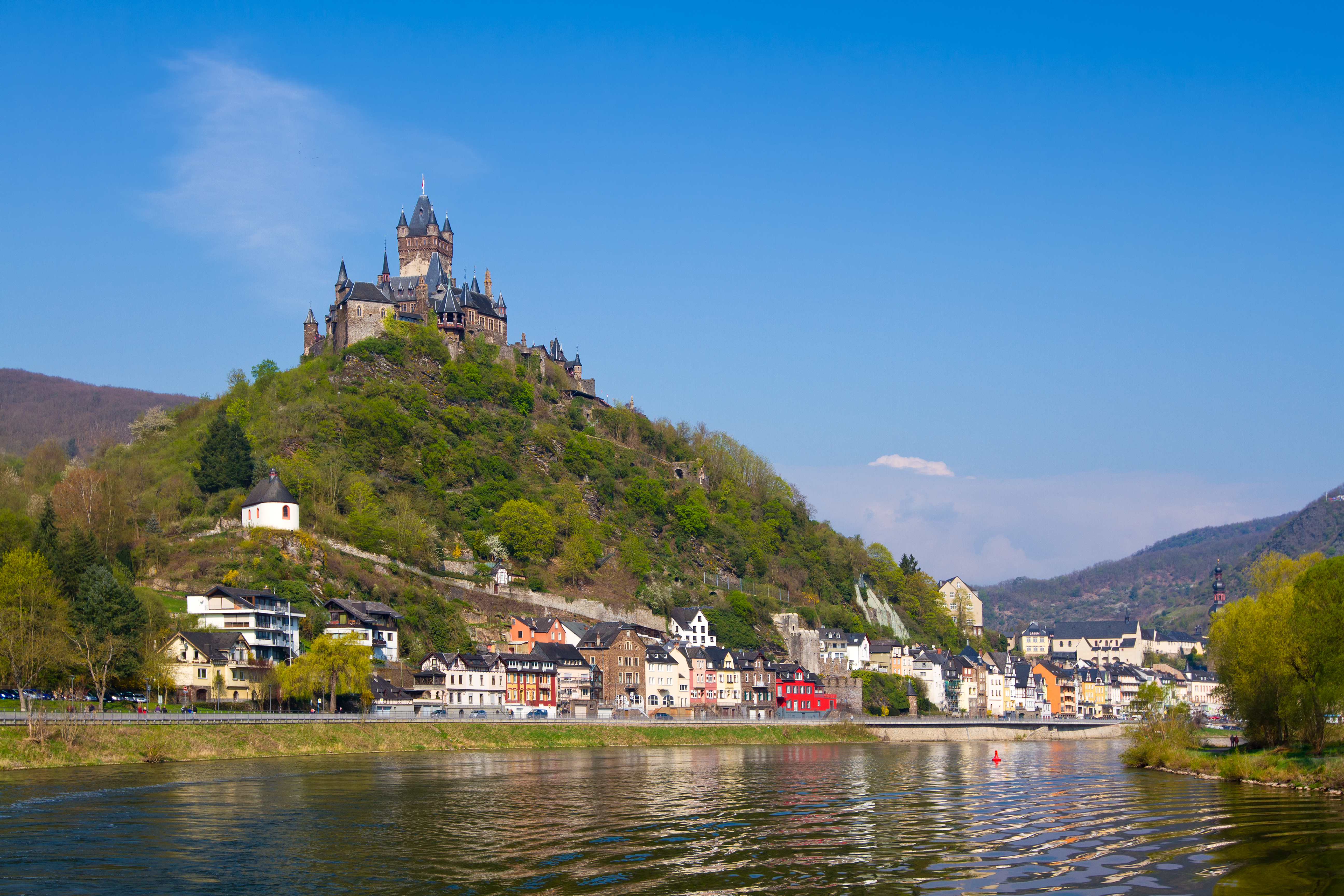 Cochem Slot på grøn bakke med farverige bindingsværkshuse langs Mosel-flodens bred