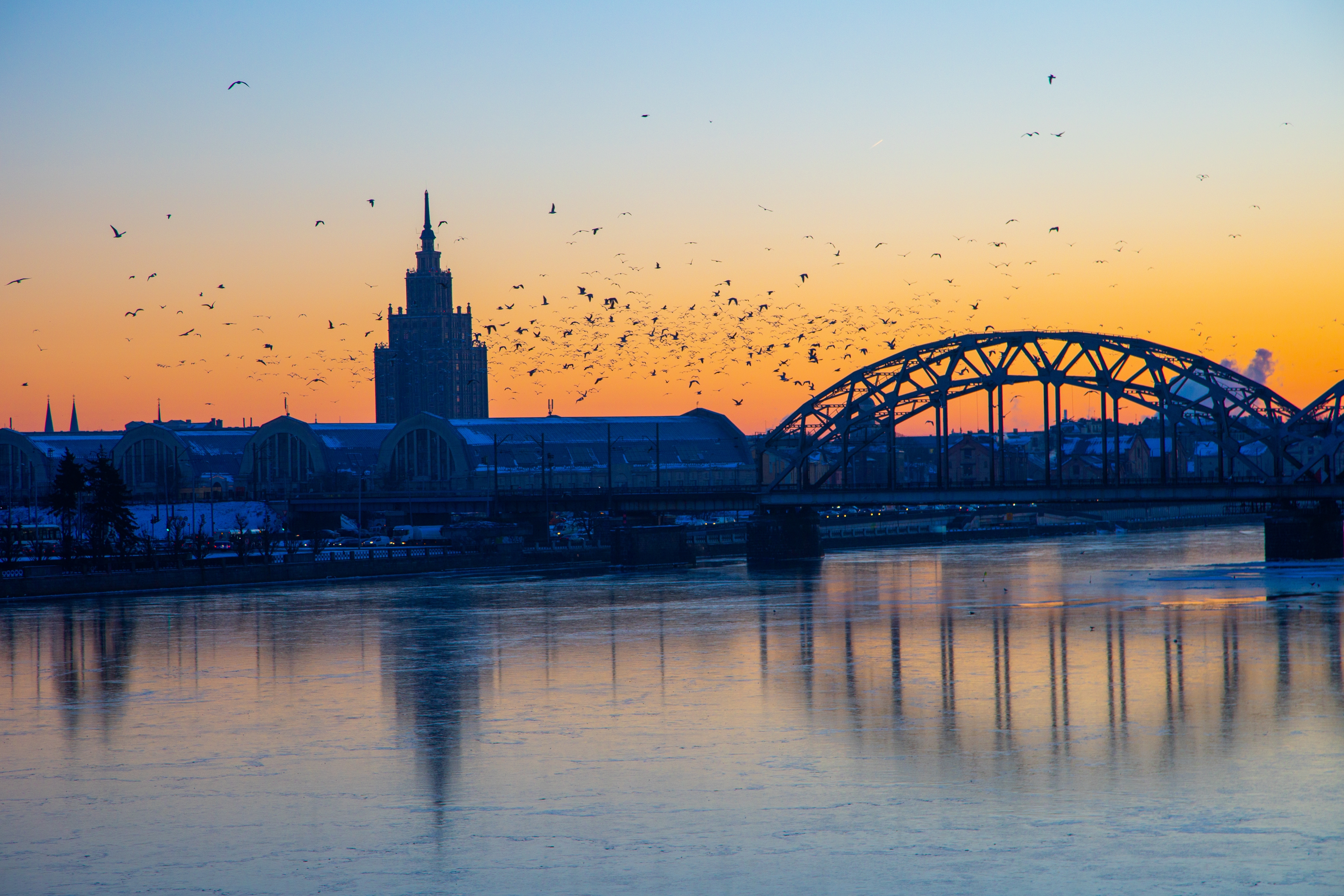 Magisk vintersolnedgang over Riga med flodreflektioner og bro