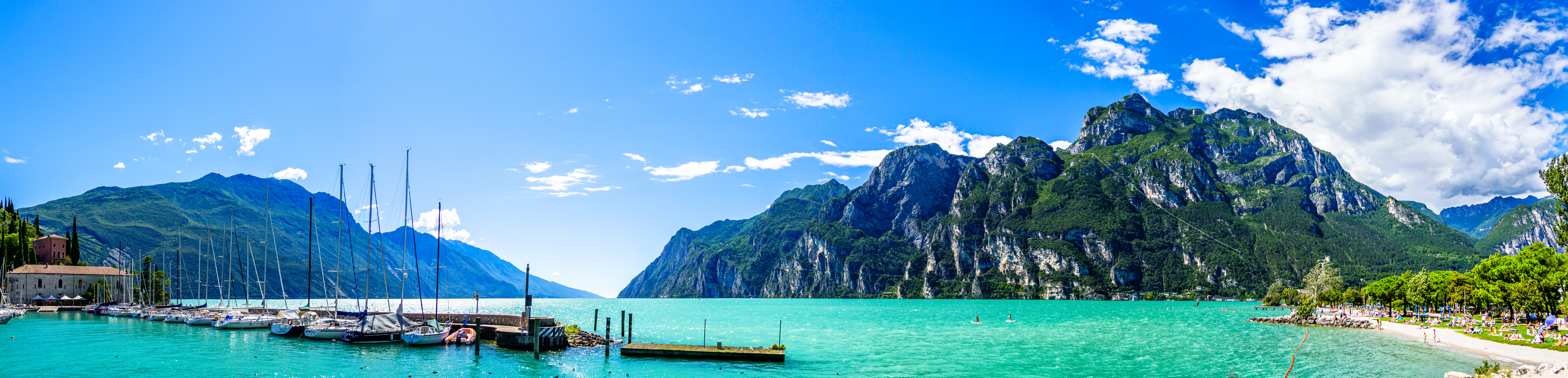 Fantastisk panoramaudsigt over Riva del Garda med krystalklart turkist vand, sejlbåde i havnen og høje bjerge i baggrunden
