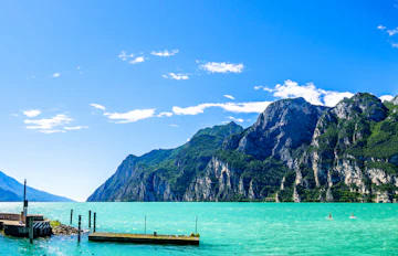 Fantastisk panoramaudsigt over Riva del Garda med krystalklart turkist vand, sejlbåde i havnen og høje bjerge i baggrunden