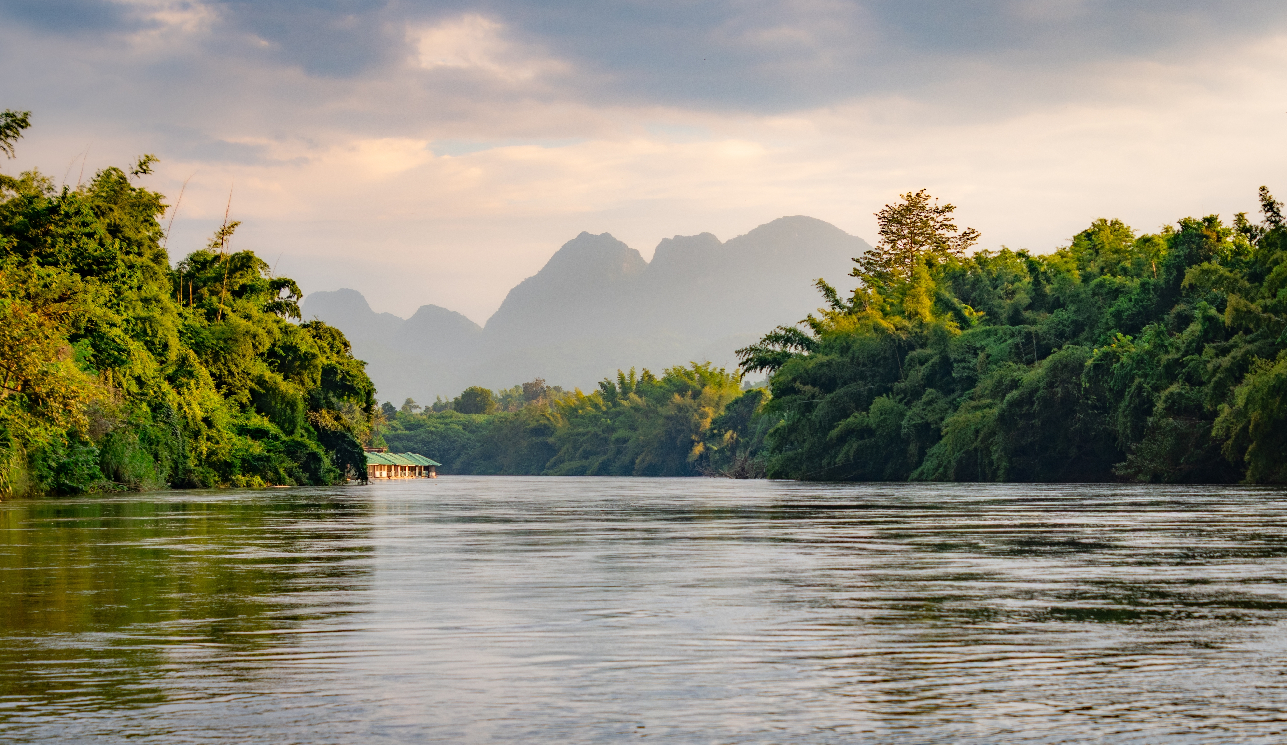 Malerisk udsigt over den berømte River Kwai i Thailand omgivet af grøn tropisk jungle og fjerne bjerge