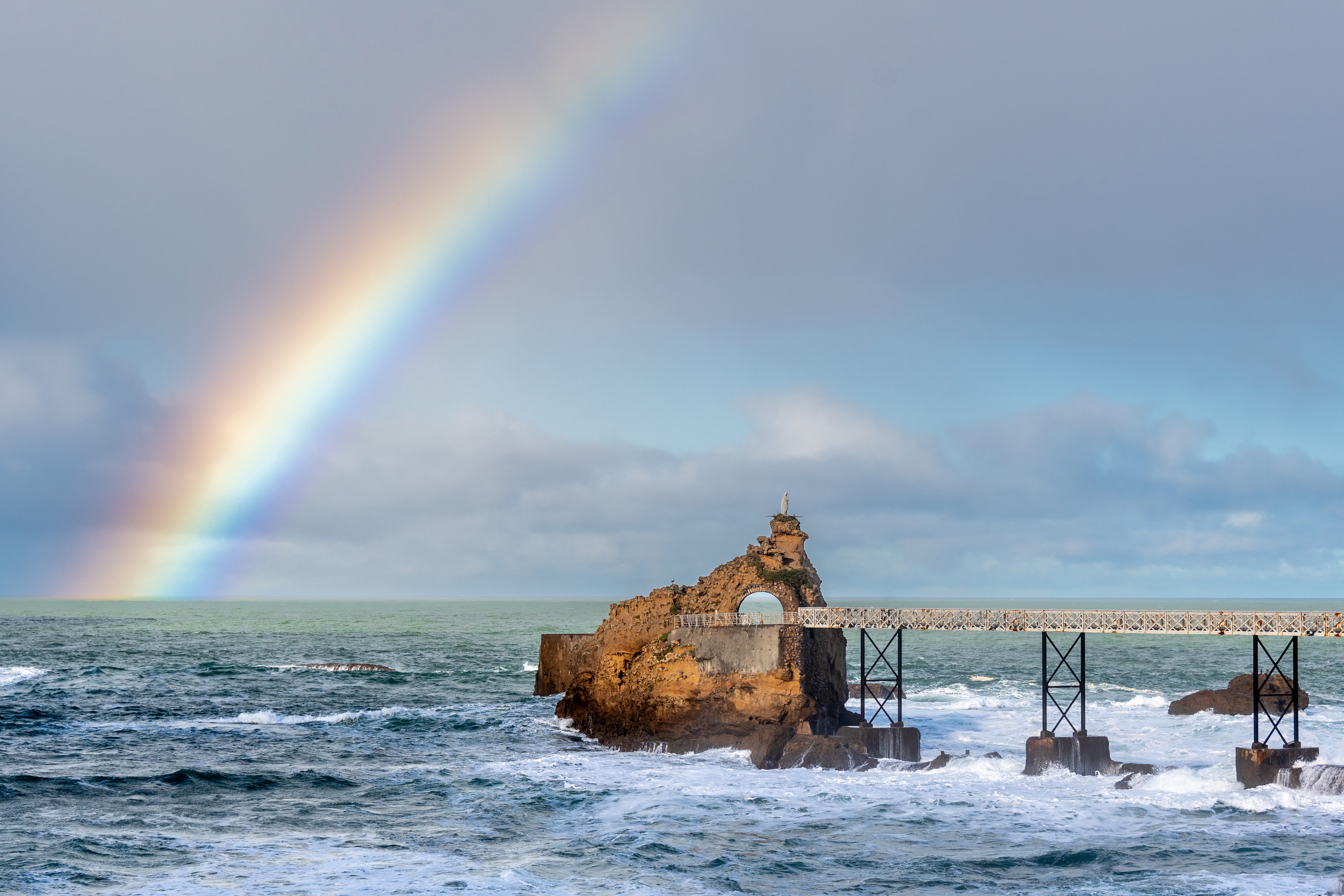 Dobbelt regnbue over Rocher de la Vierge klippen i Biarritz med kraftige Atlanterhavet bølger