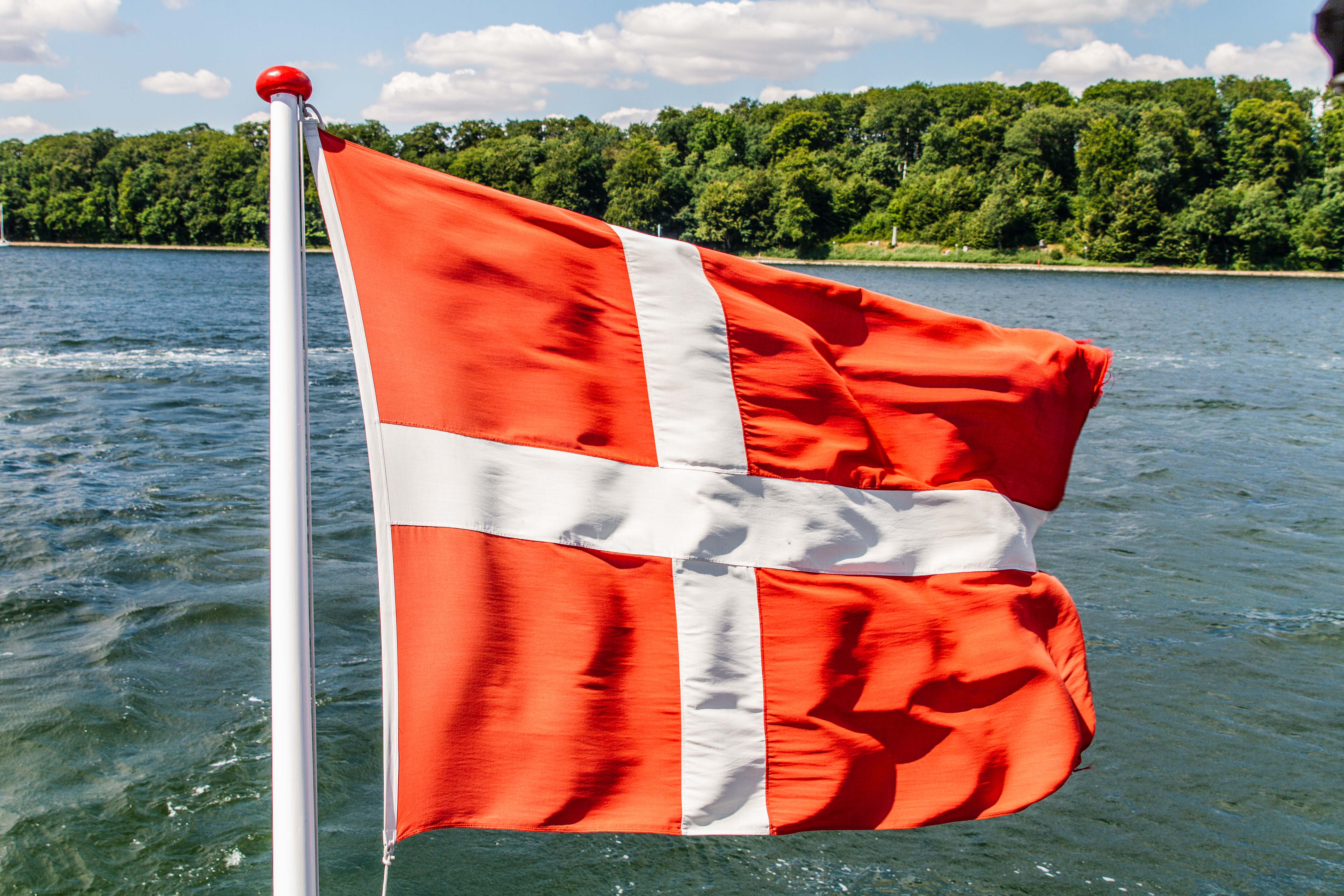 Rødt og hvidt dansk flag vajende på båd langs Danmarks kyst