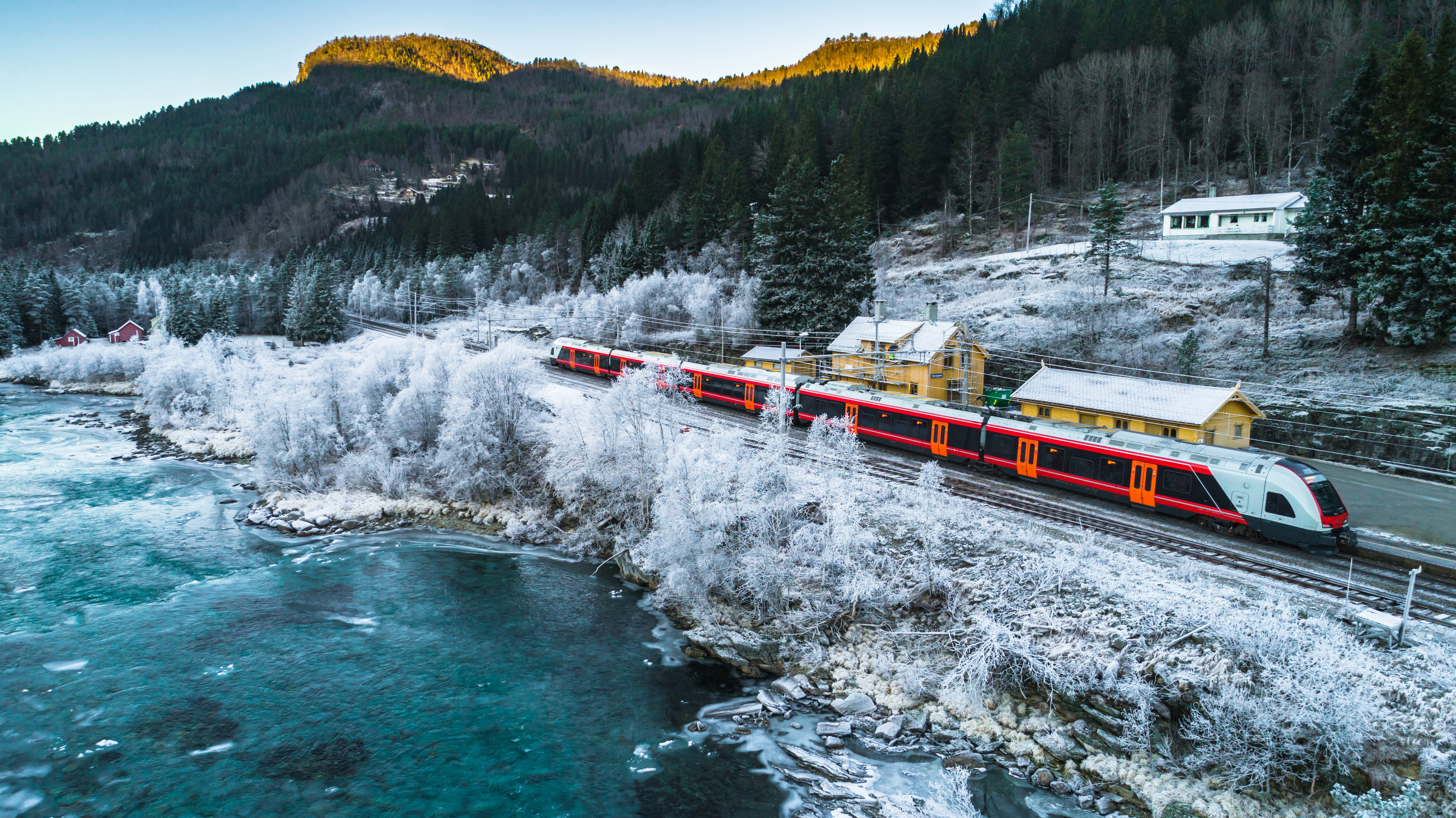 Rødt passagertog i Norge kører gennem smukt vinterlandskab med sne og is