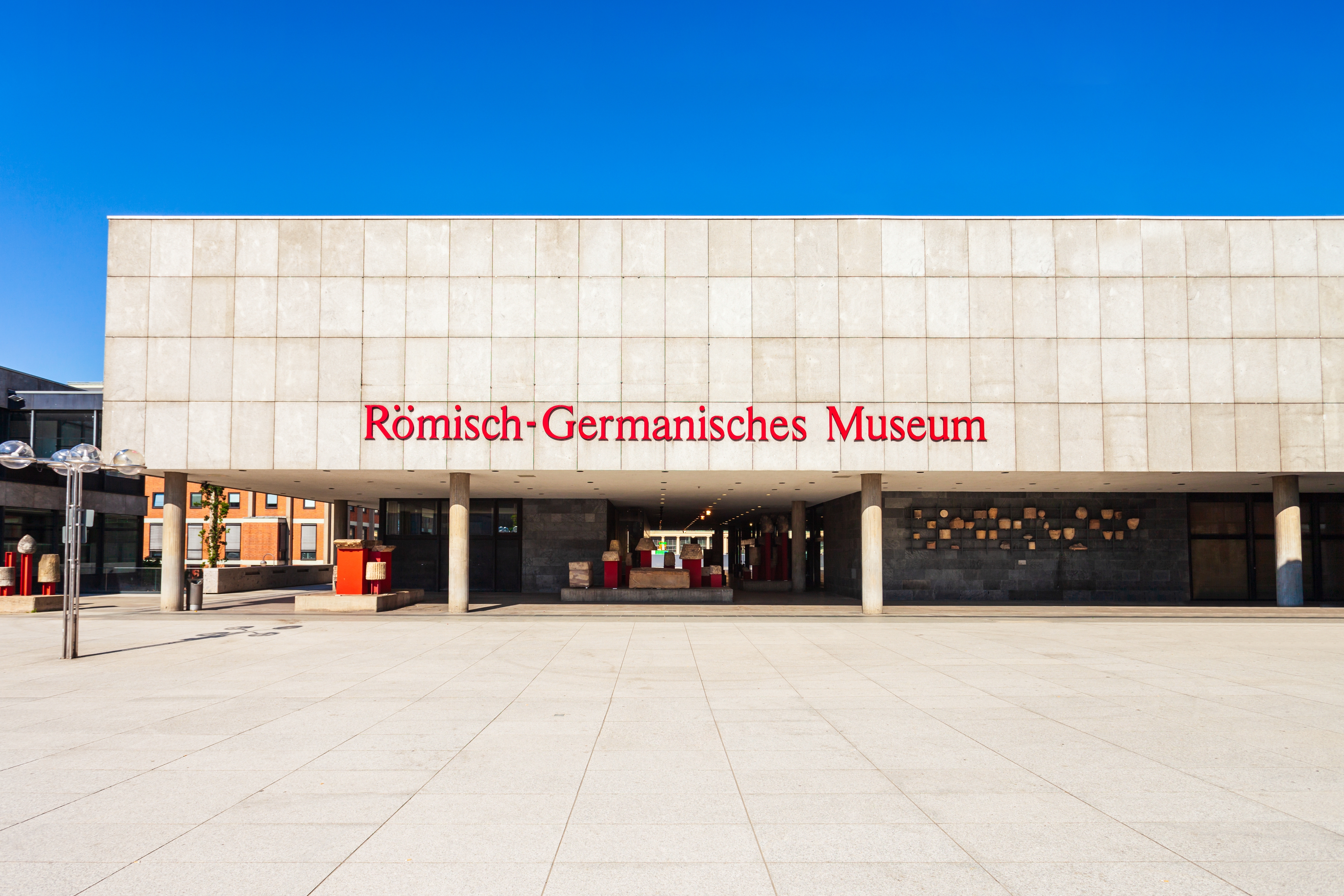Römisch-Germanisches Museum i Køln, Tyskland, med sin markante moderne bygning og røde museumsskilt under blå himmel