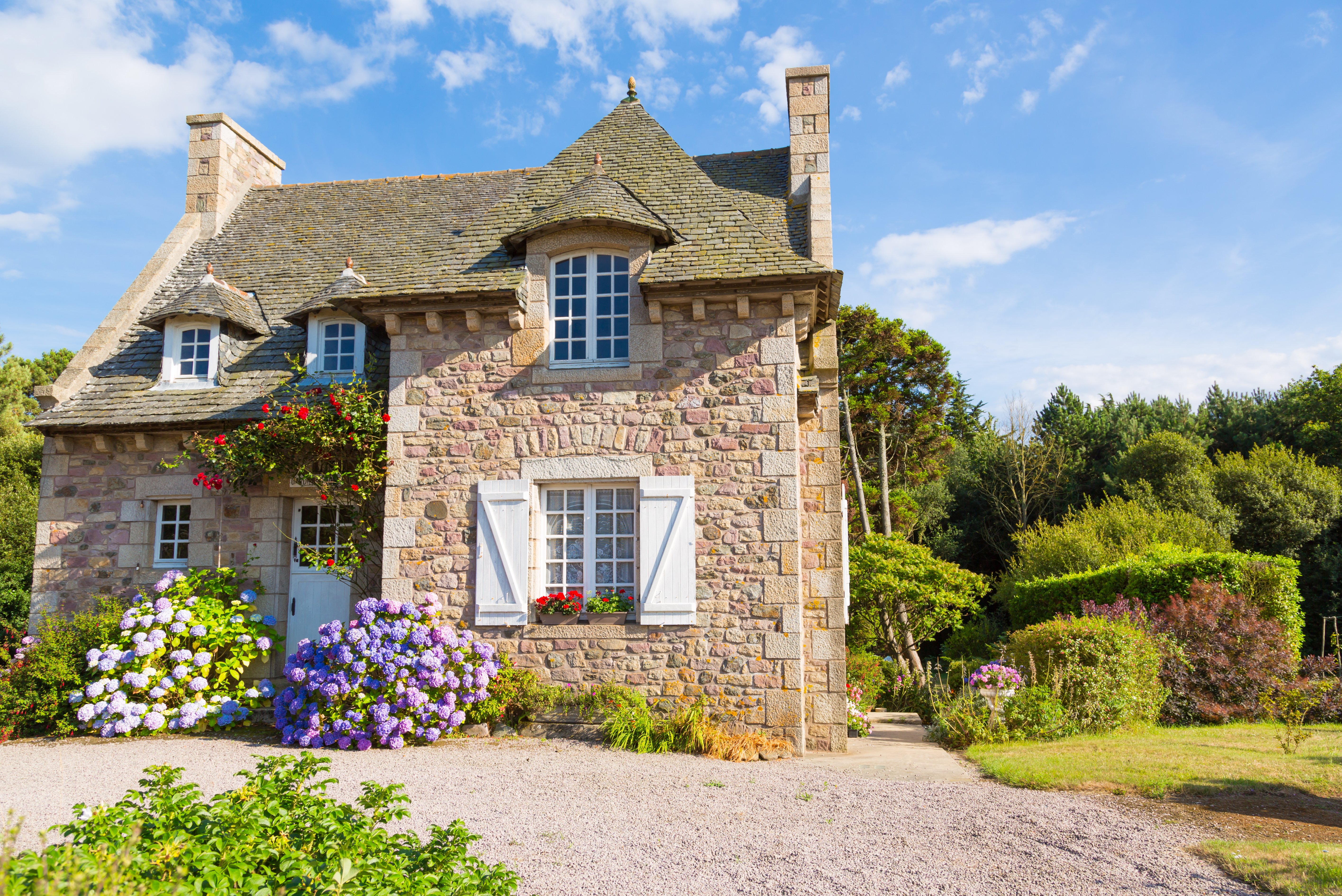 Romantisk fransk landhus i Bretagne bygget af natursten med blomstrende blå hortensiaer og velplejet have