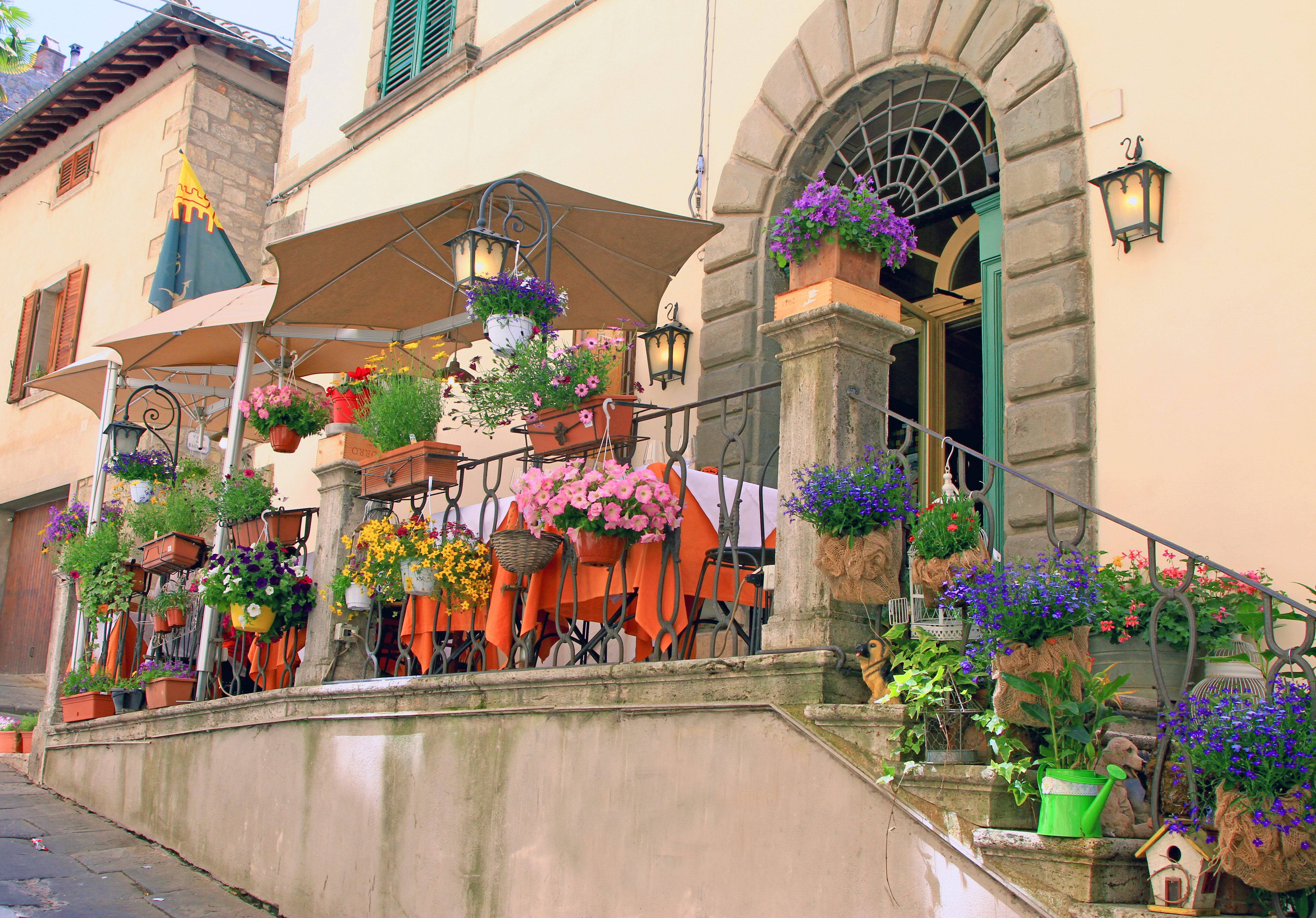 Romantisk restaurant med blomsterprydede trapper og orange duge på terrassen i den historiske by Cortona, Toscana