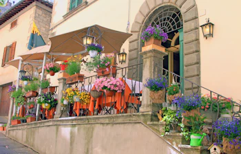 Romantisk restaurant med blomsterprydede trapper og orange duge på terrassen i den historiske by Cortona, Toscana