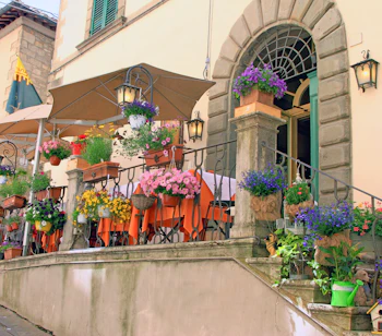 Romantisk restaurant med blomsterprydede trapper og orange duge på terrassen i den historiske by Cortona, Toscana