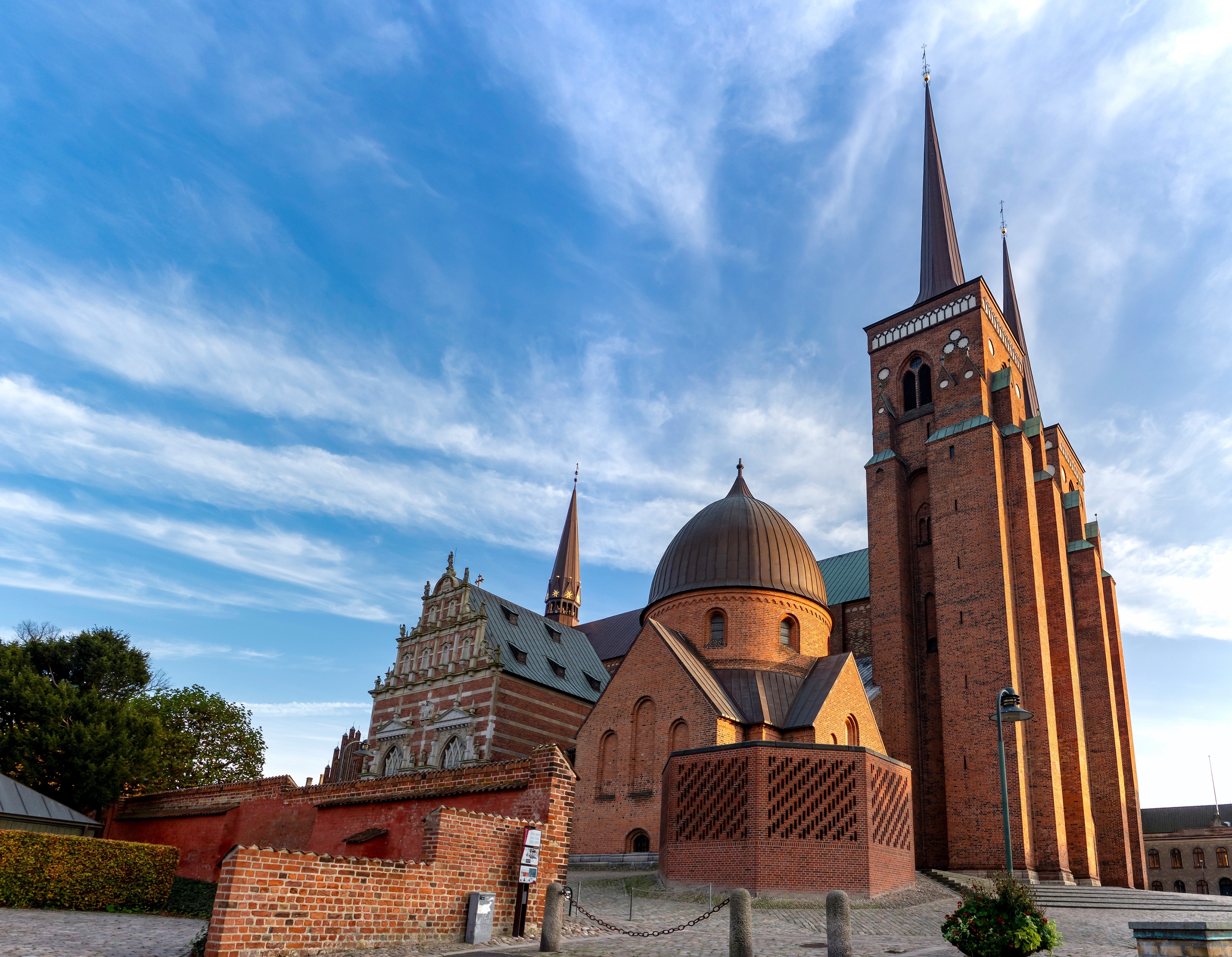 Vidvinkelvisning af Roskilde Domkirke i Danmark med smukke røde murstenstårne og blå himmel ved solnedgang
