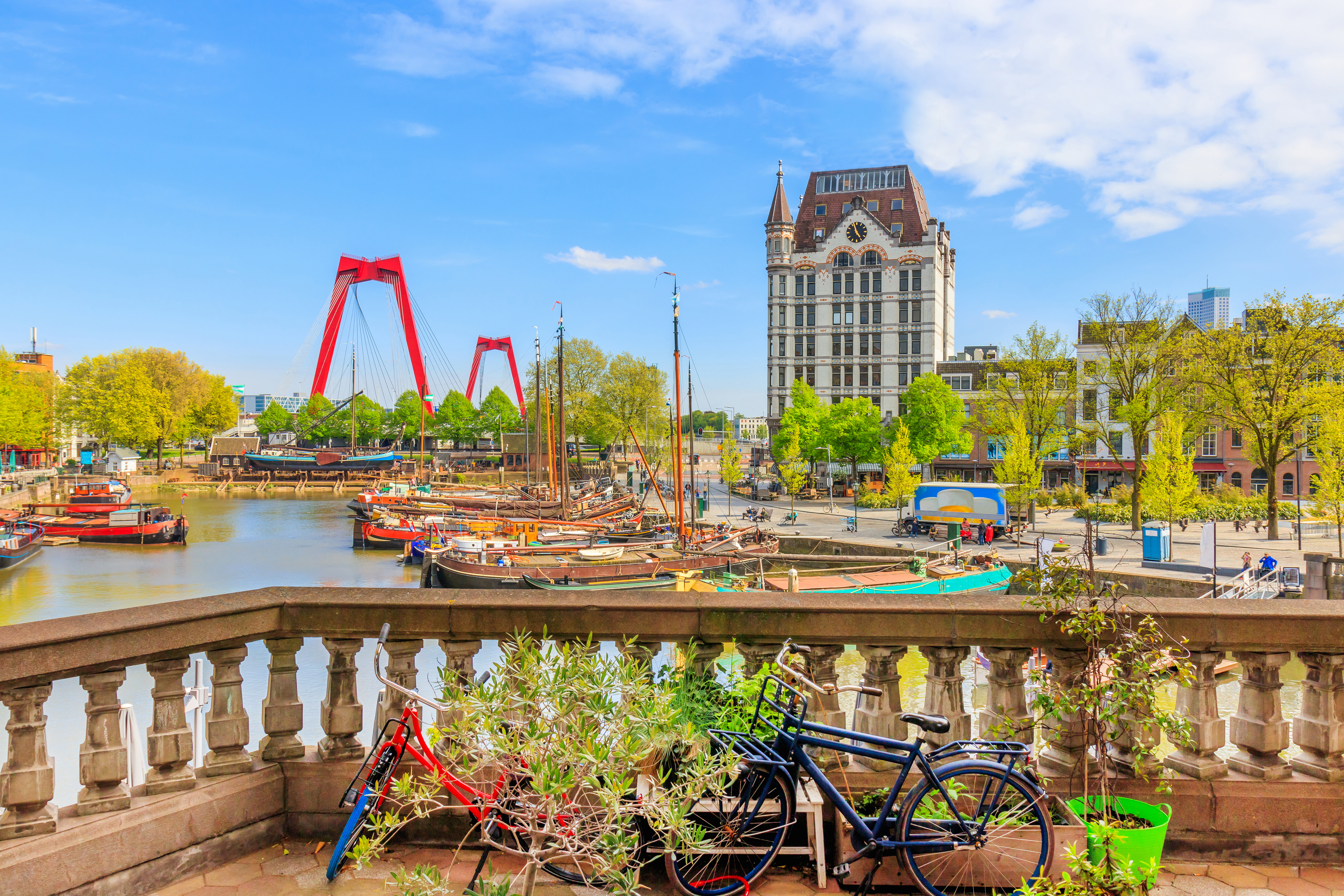 Malerisk udsigt over Rotterdams gamle havn med den ikoniske røde Willemsbrug, traditionelle både og historiske bygninger under blå himmel i Holland