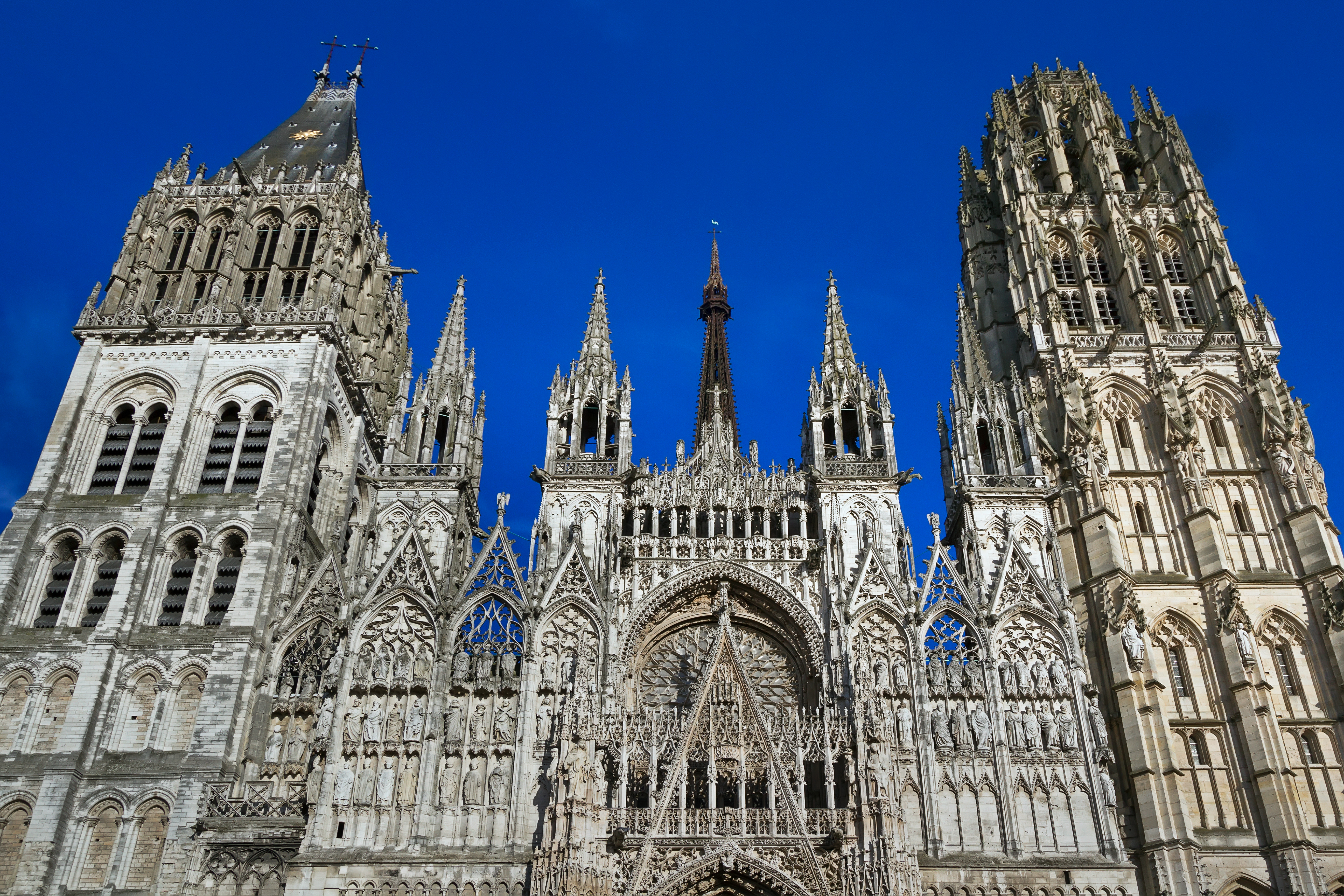 Storslået gotisk katedral i Rouen, Normandiet med ornamenterede stentårne og historisk facade mod strålende blå himmel