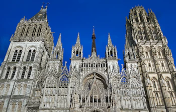 Storslået gotisk katedral i Rouen, Normandiet med ornamenterede stentårne og historisk facade mod strålende blå himmel