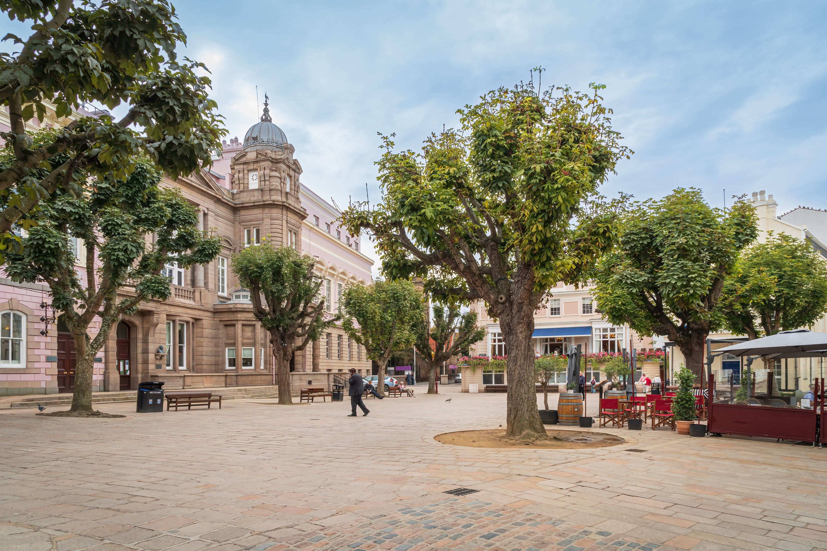 Idyllisk Royal Square i St Helier på kanaloen Jersey med sandstensbyggerier og café under træerne