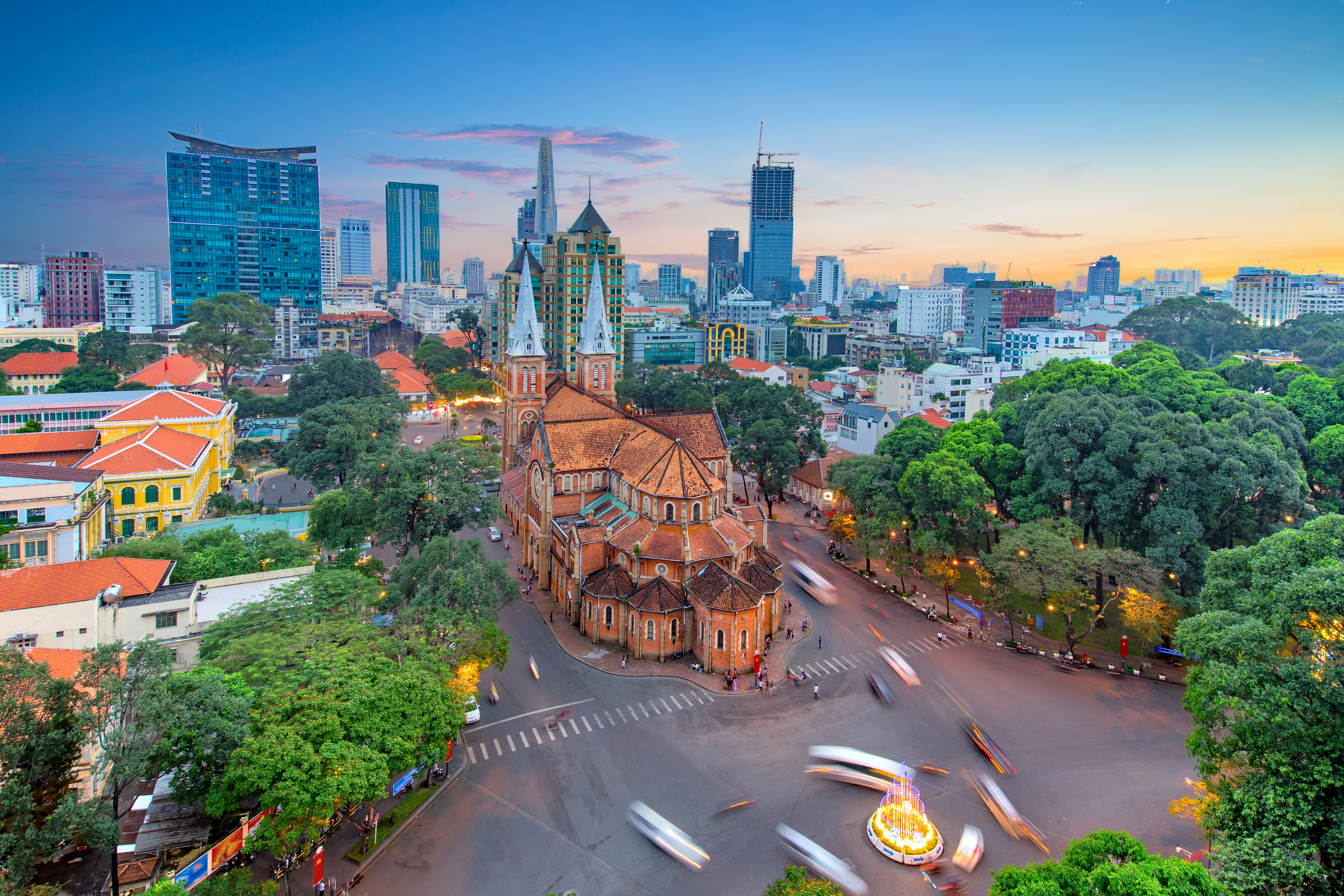 Ikonisk Notre-Dame Basilika i Saigon fotograferet fra luften ved solnedgang med Ho Chi Minh Citys moderne skyline, Vietnam