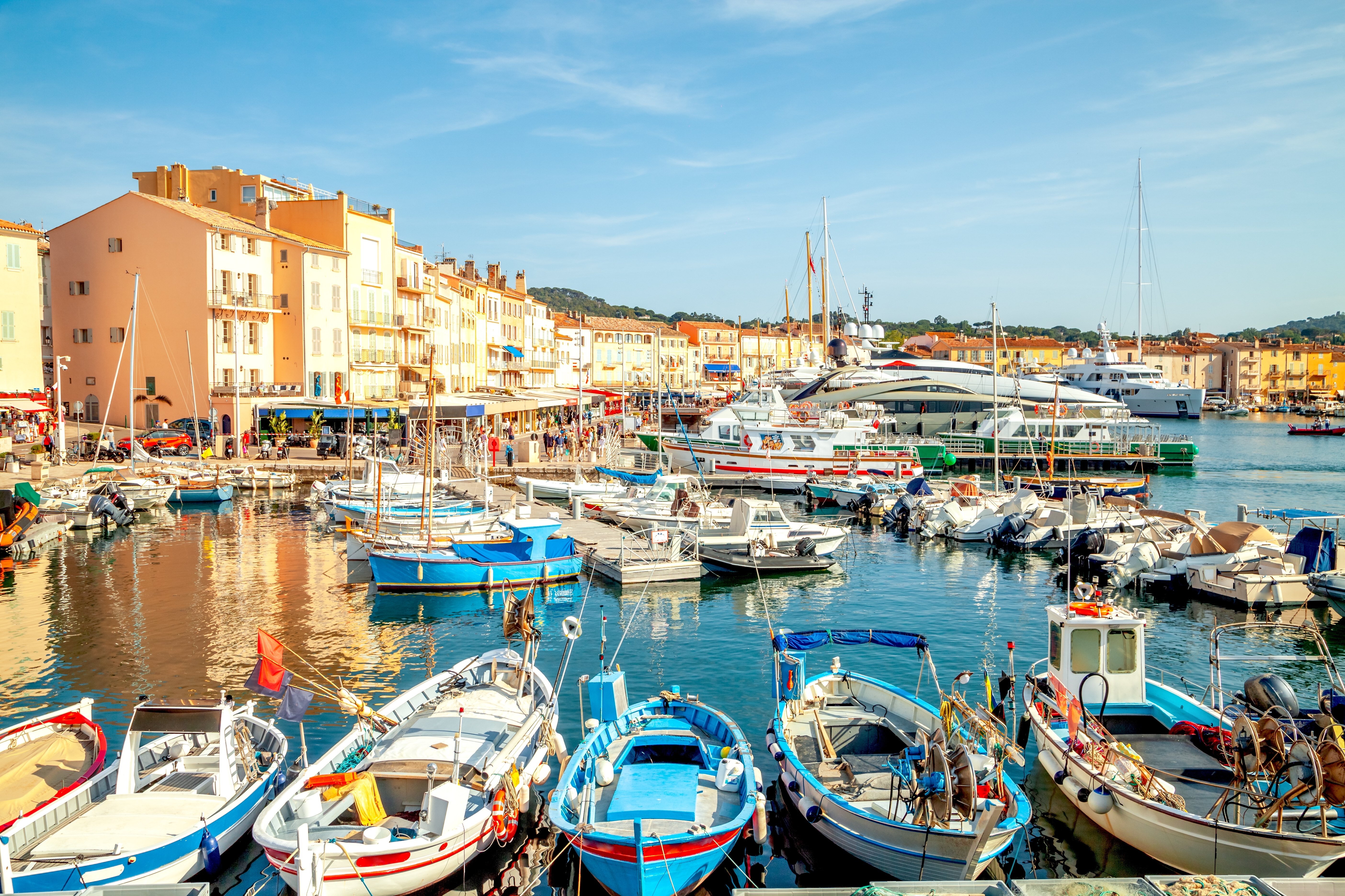 Idyllisk havn i Saint-Tropez med blå fiskerbåde og pastelfarvet bymidte spejlet i det rolige havnevand på Côte d'Azur