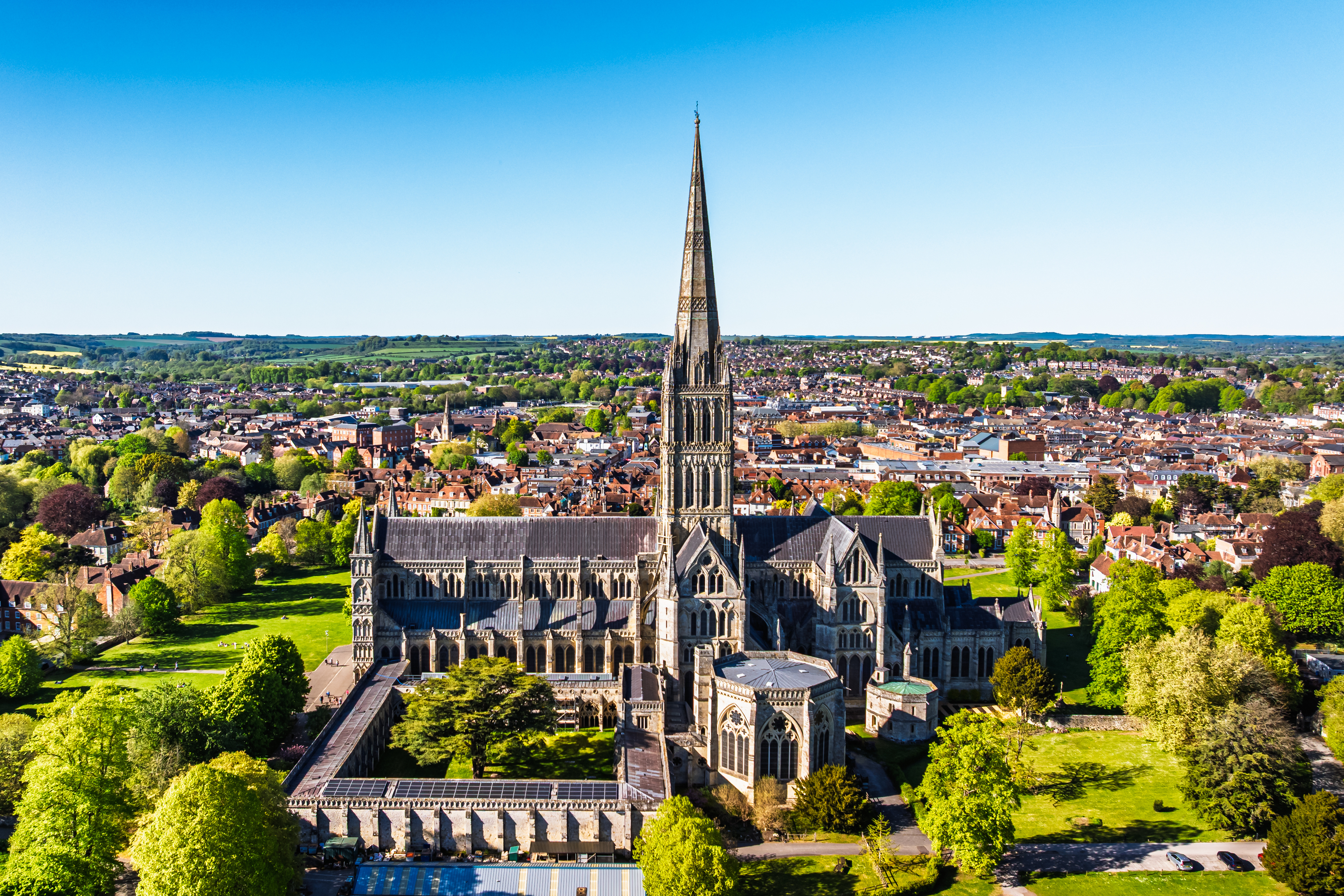 Spektakulært luftfoto af Salisbury Cathedral med det høje gotiske spir omgivet af grønne træer i Salisbury, Wiltshire