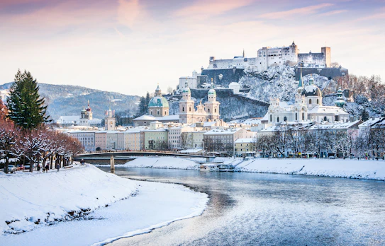 Vinteridyl i Salzburg med den historiske Hohensalzburg-fæstning og Salzach-floden under et snedækket landskab, Østrig