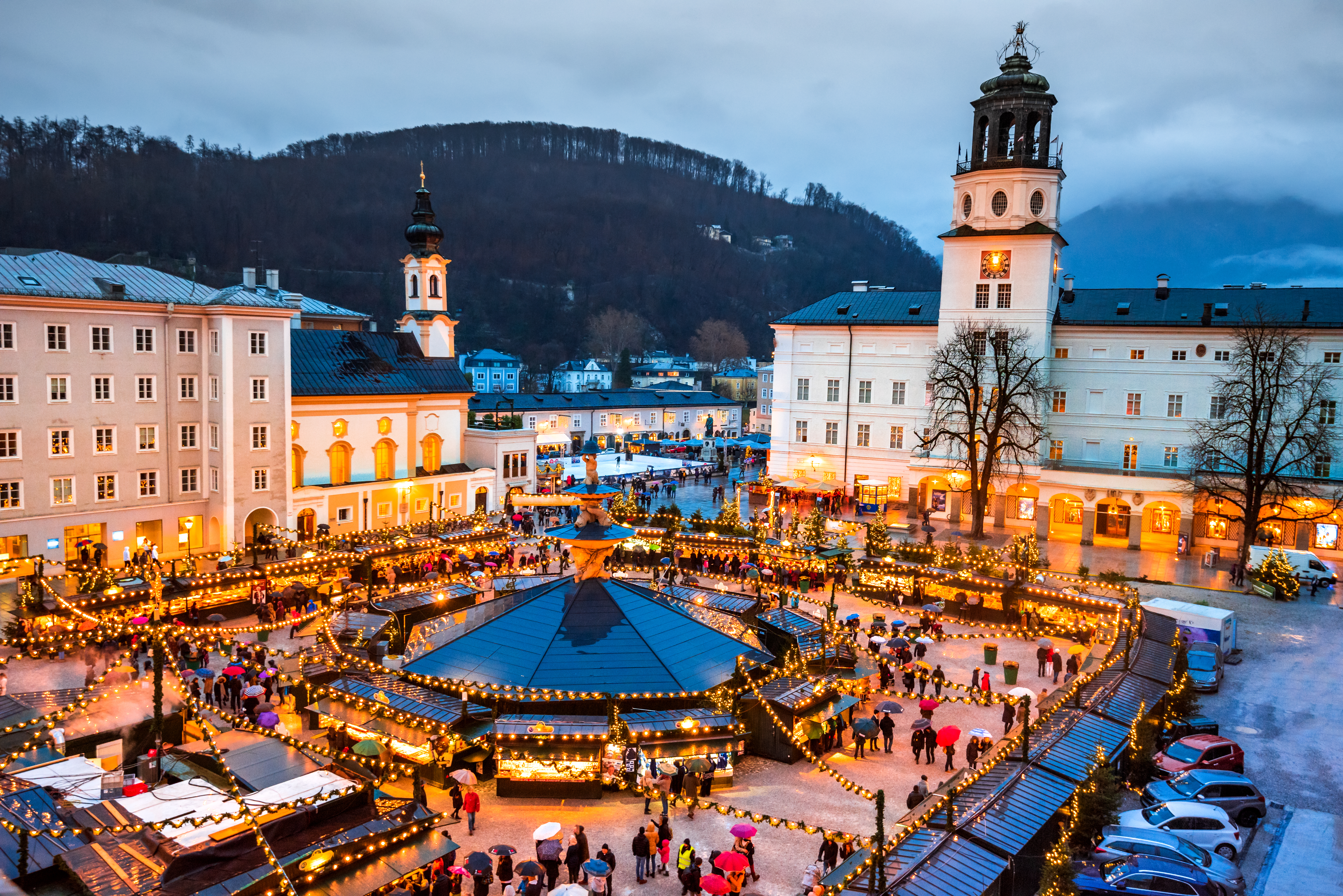 Panoramaudsigt over det traditionsrige julemarked ved Domkirken i Salzburg, med festlige boder og julelys der skaber en magisk stemning i aftenmørket