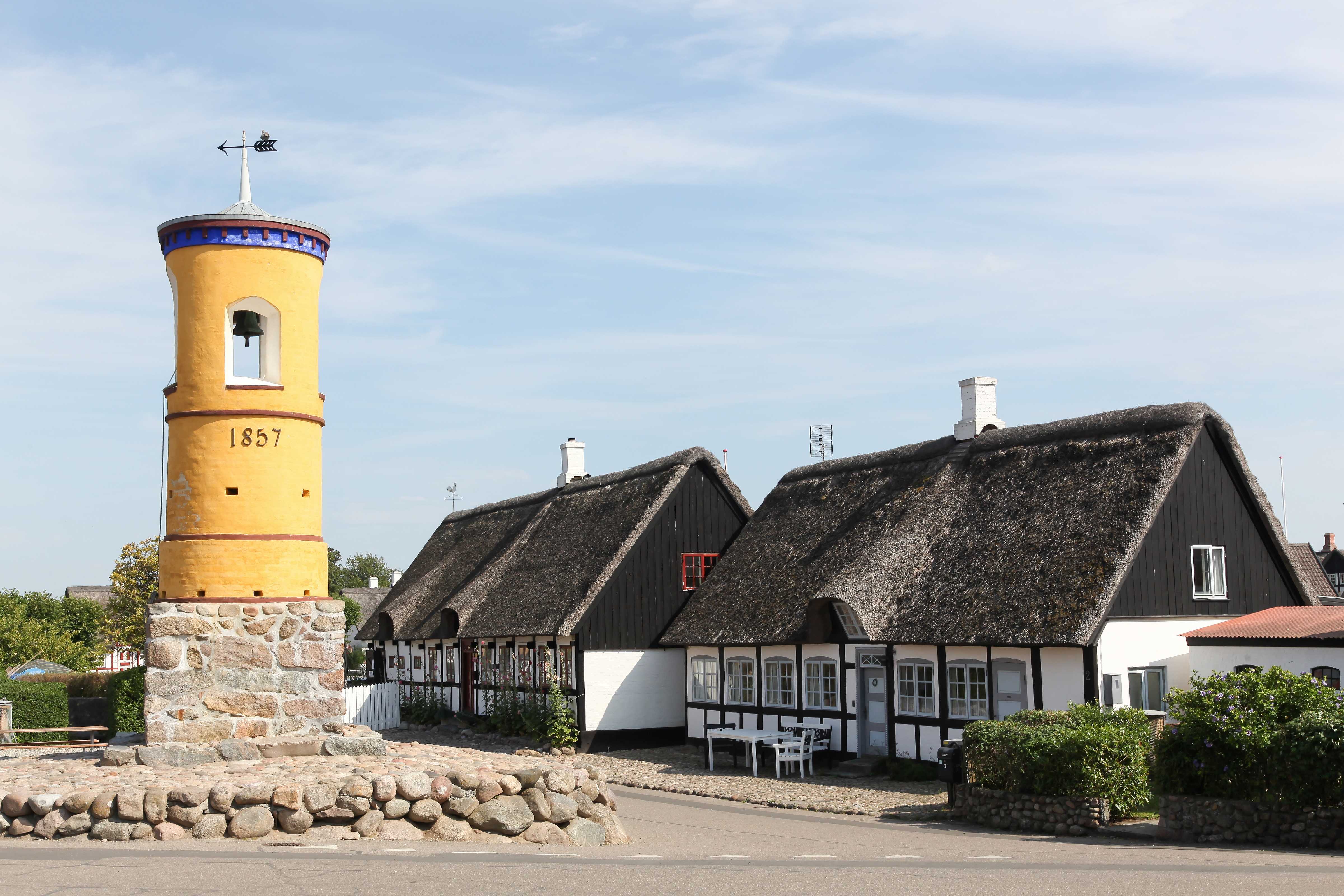 Idyllisk sommerstemning i Nordby på Samsø med det gule klokketa rn fra 1857 og traditionelle danske stråta gte huse