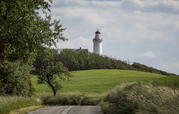 Naturskøn landevej omgivet af grønne marker der fører til det historiske Vesborg Fyr på Samsøs sydlige spids, en perfekt destination for en sommerudflugt
