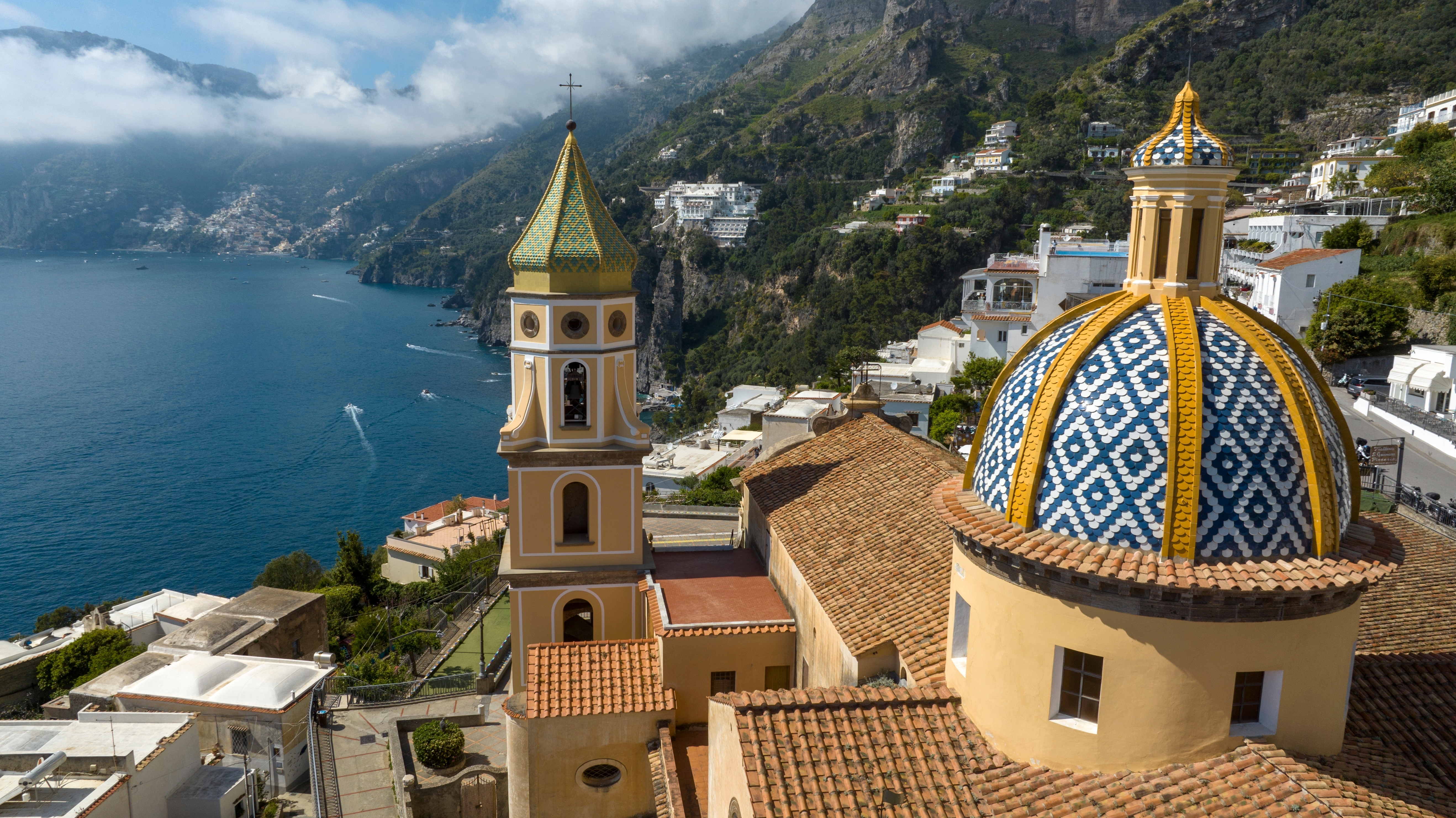 Dronefoto af den smukke San Gennaro kirke i Praiano med dens ikoniske keramiske kuppel og klokketårn mod den blå Amalfikyst i Italien