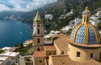 Dronefoto af den smukke San Gennaro kirke i Praiano med dens ikoniske keramiske kuppel og klokketårn mod den blå Amalfikyst i Italien