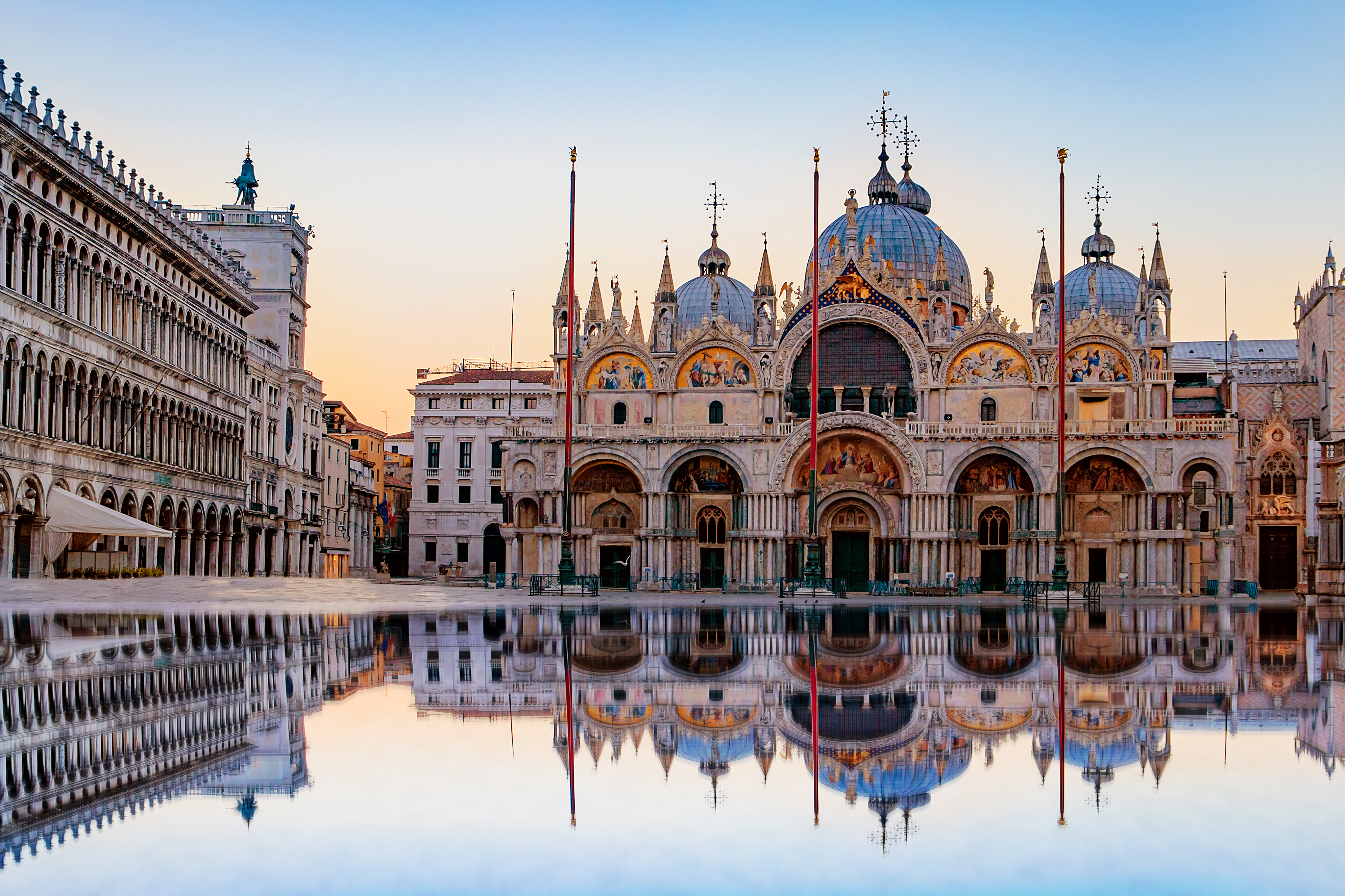 Markuskirkens byzantinske arkitektur badet i gyldent morgenlys med spejling i vandet på pladsen i Venedig