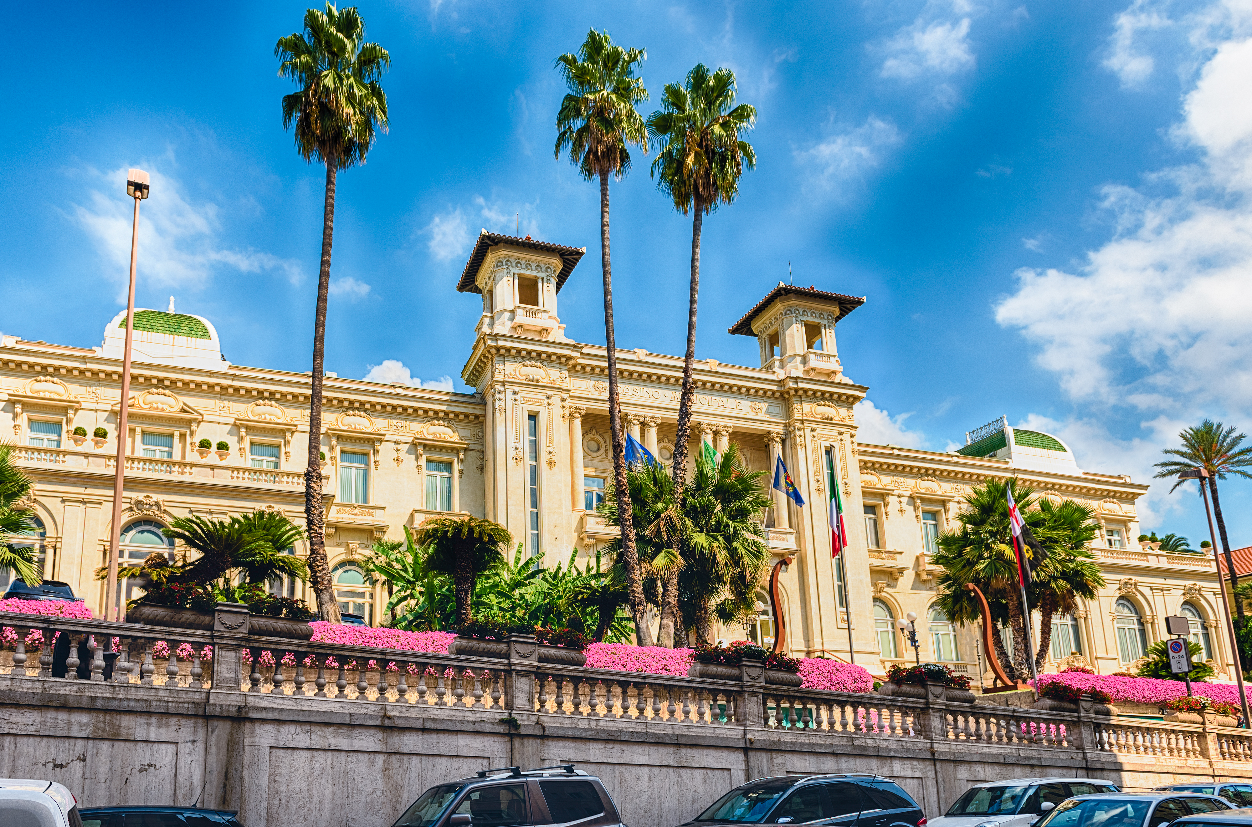 Det ikoniske Casino i Sanremo, Italien, med høje palmer og farverige blomster foran den historiske gule bygning