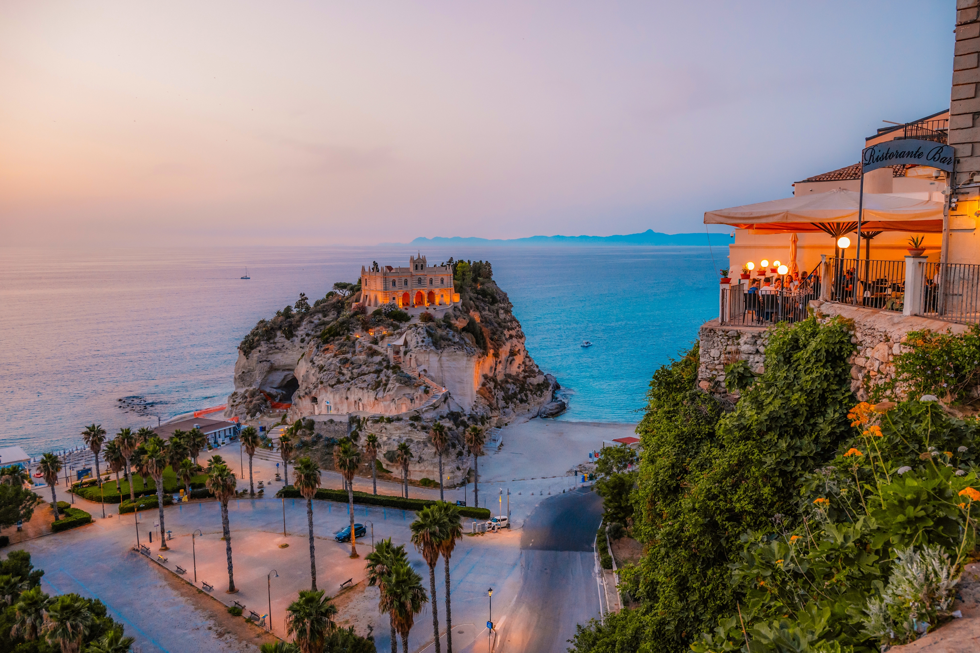 Magisk aftenstemning ved Santa Maria dell'Isola kirken i Tropea, Calabrien, med palmer langs promenaden og det smukke Middelhav