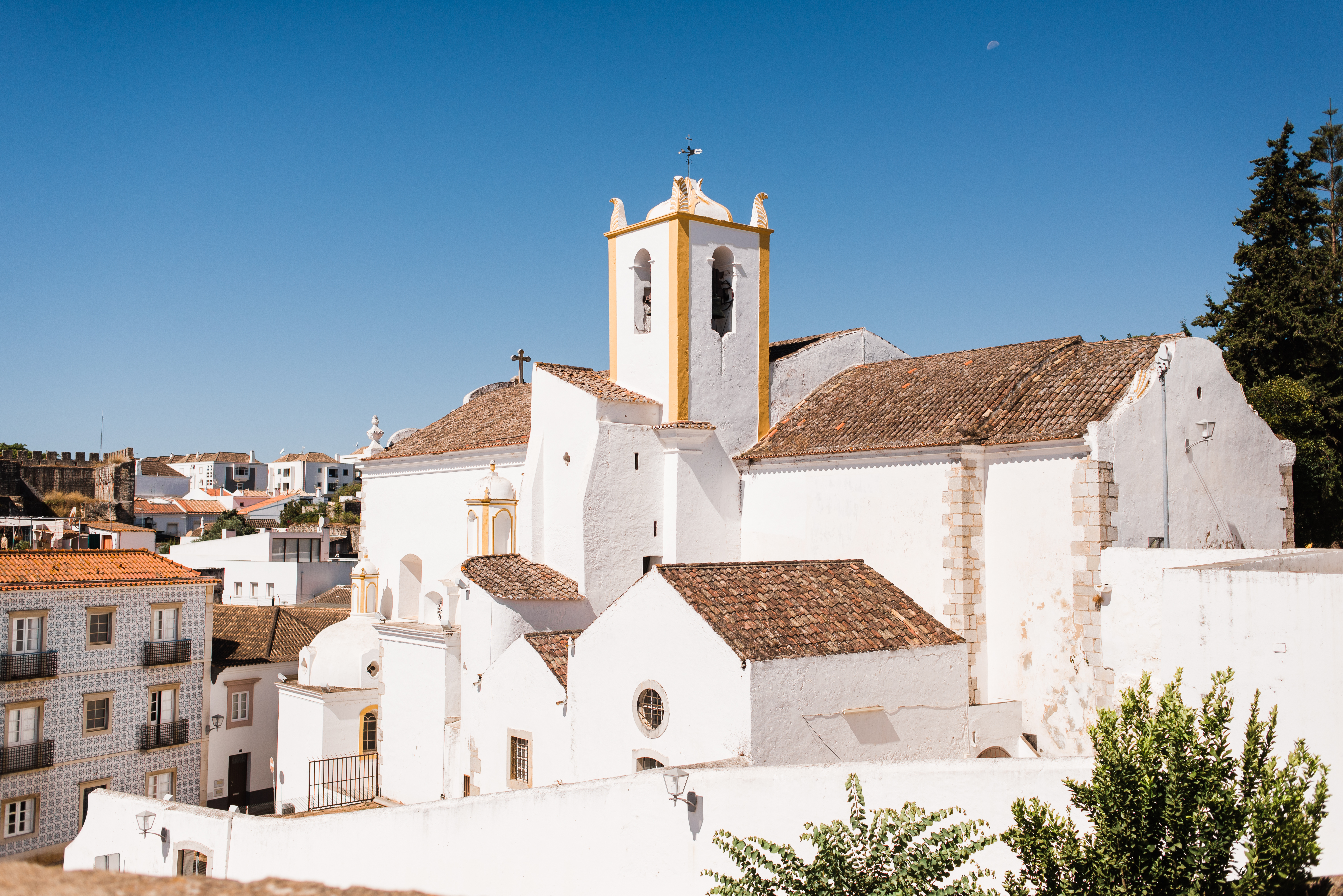 Historisk Santiago Kirke i Taviras gamle bydel med karakteristisk gult klokketårn og hvidkalkede bygninger under blå himmel i Algarve, Portugal
