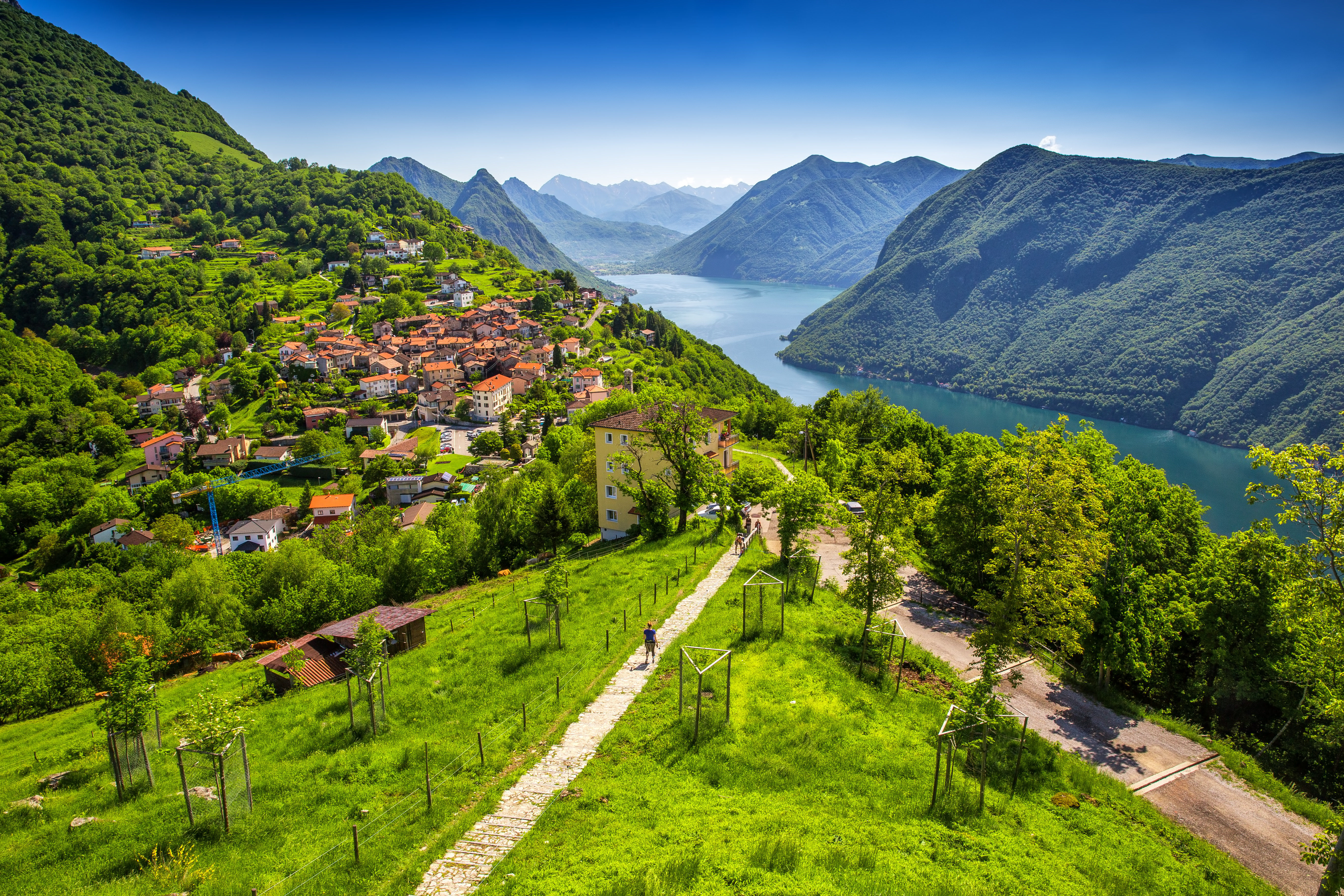 Idyllisk panorama fra Monte Bre med udsigt over Lugano by og sø, grønne bjerge og klart blåt vand i Ticino-regionen, Schweiz