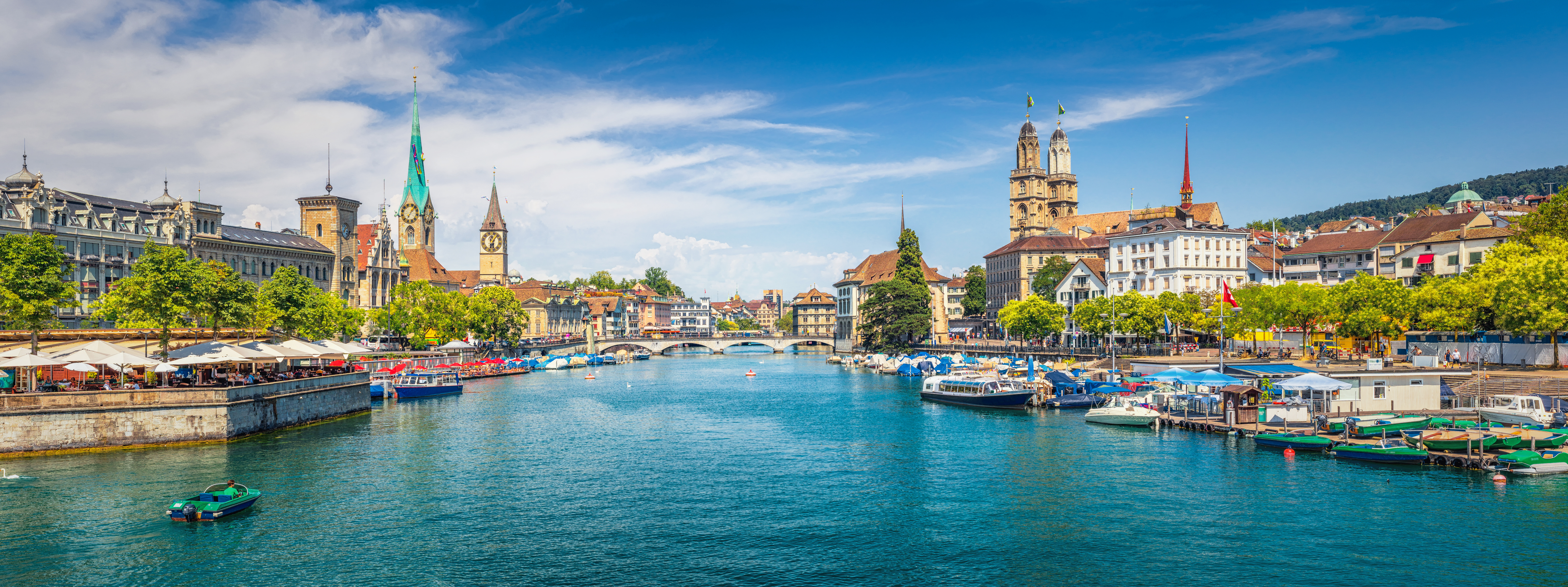 Zürichs charmerende gamle bydel med kirketårne og maritime aktiviteter ved Limmat-floden under blå himmel