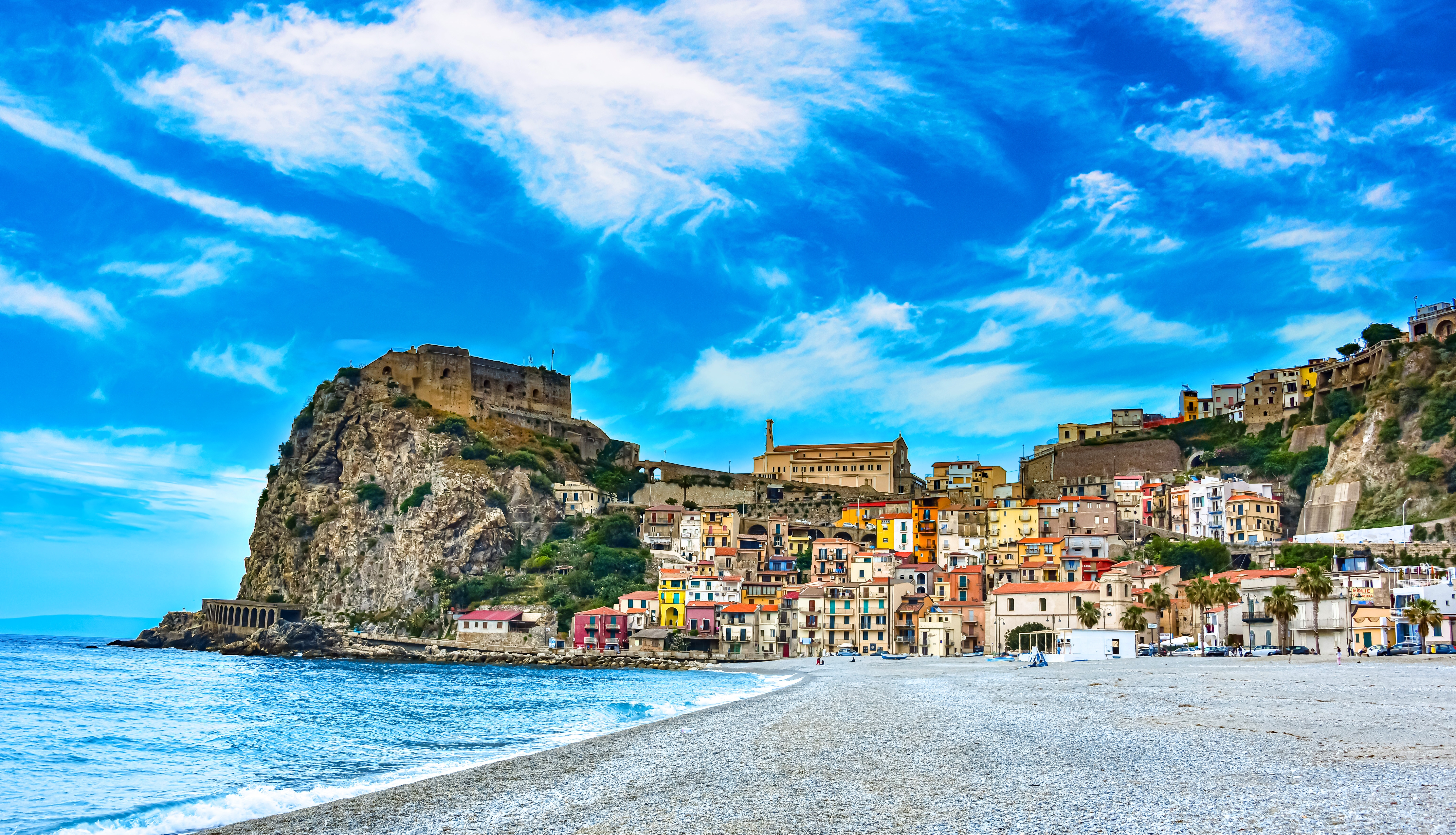 Idyllisk strand i Scilla ved Reggio Calabria med farverige huse og middelalderborg på klippeskrænt i solskin
