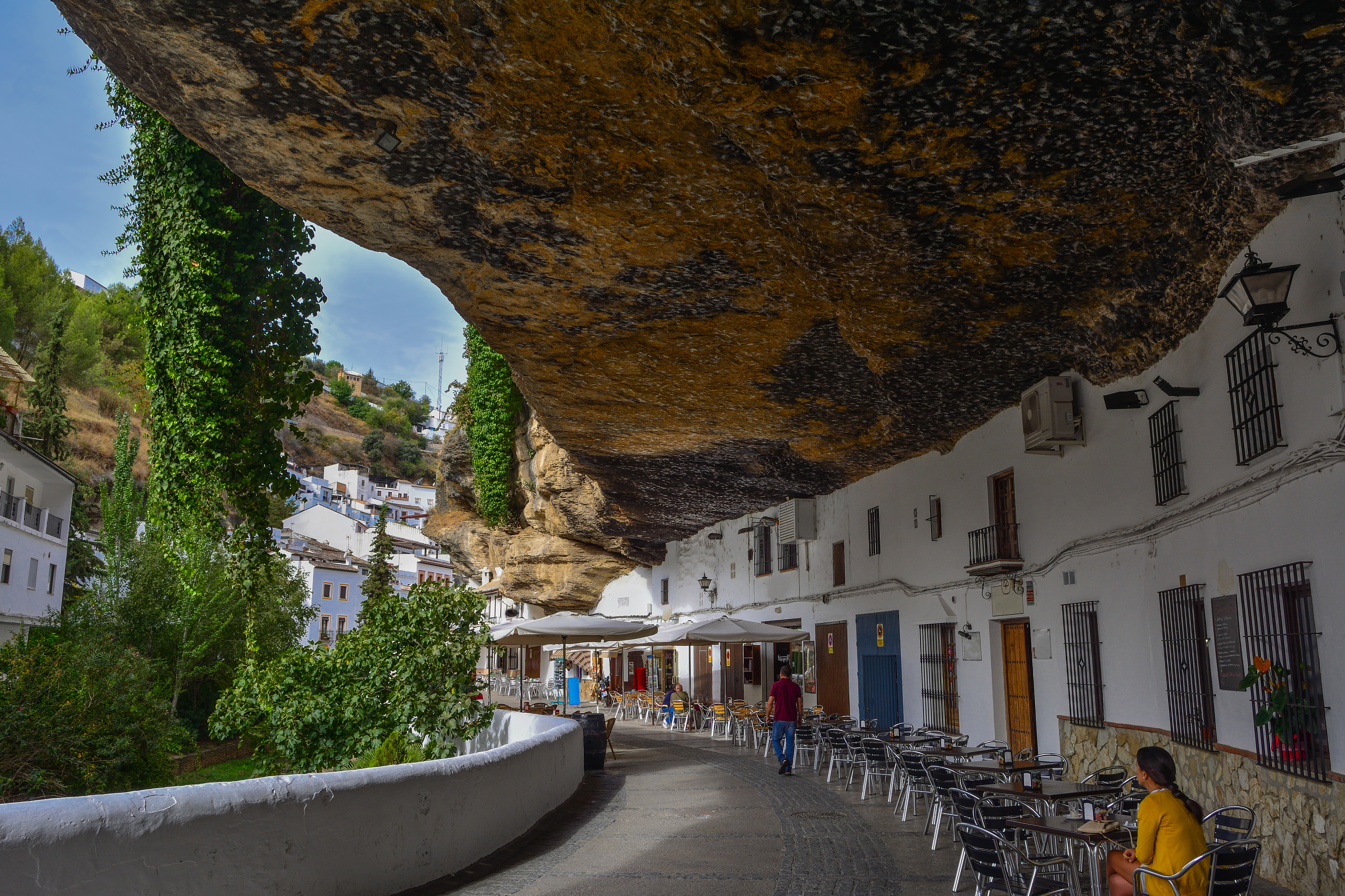 Unik gadestemning i Setenil de las Bodegas, Spanien, med caféborde under den imponerende klippeformation og karakteristiske hvide huse