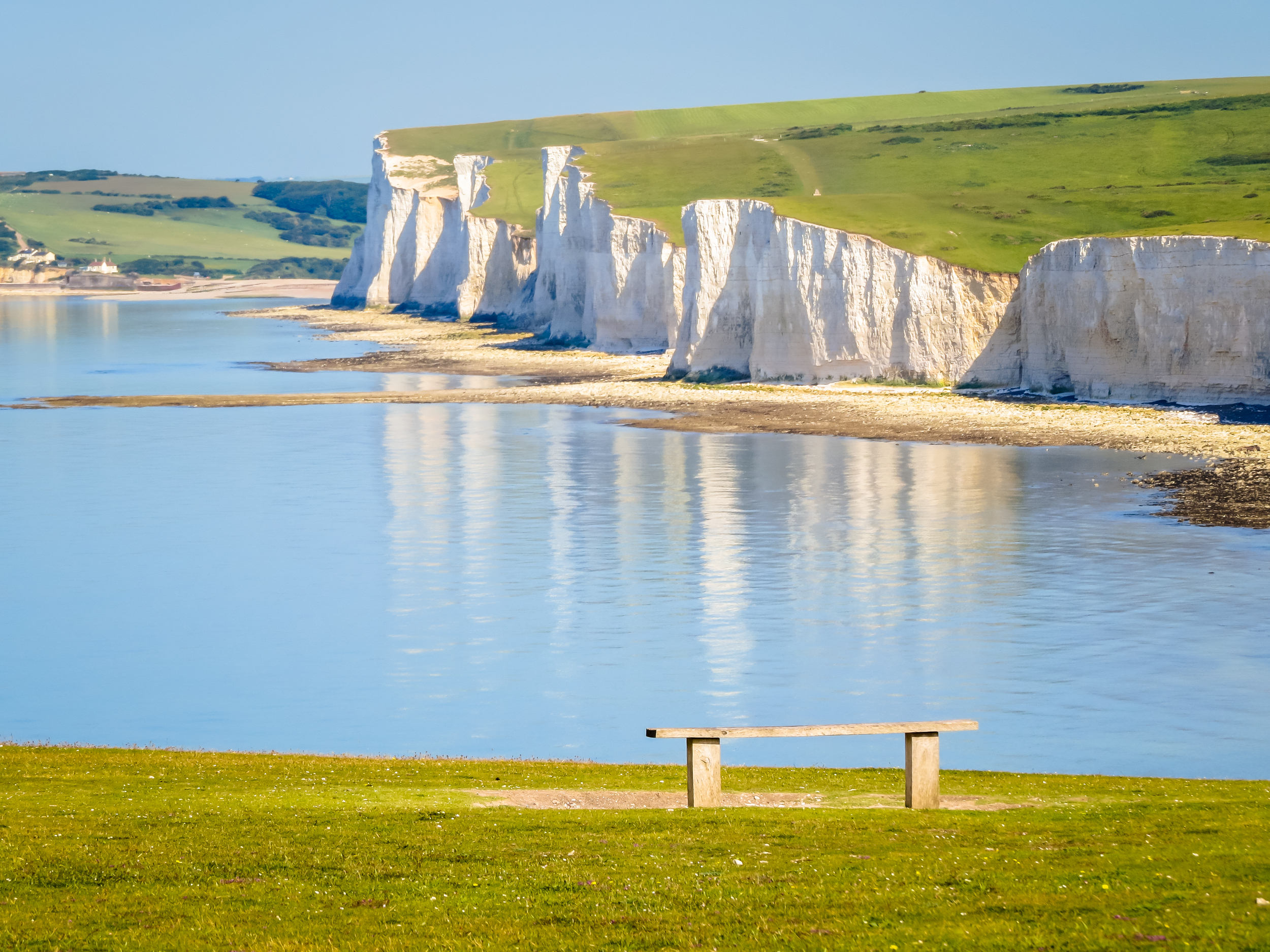 De majestætiske Seven Sisters hvide kridtklipper ved Cuckmere Haven i East Sussex, England, med en fredfyldt udsigt over det rolige hav og grønne marker på en smuk sommerdag