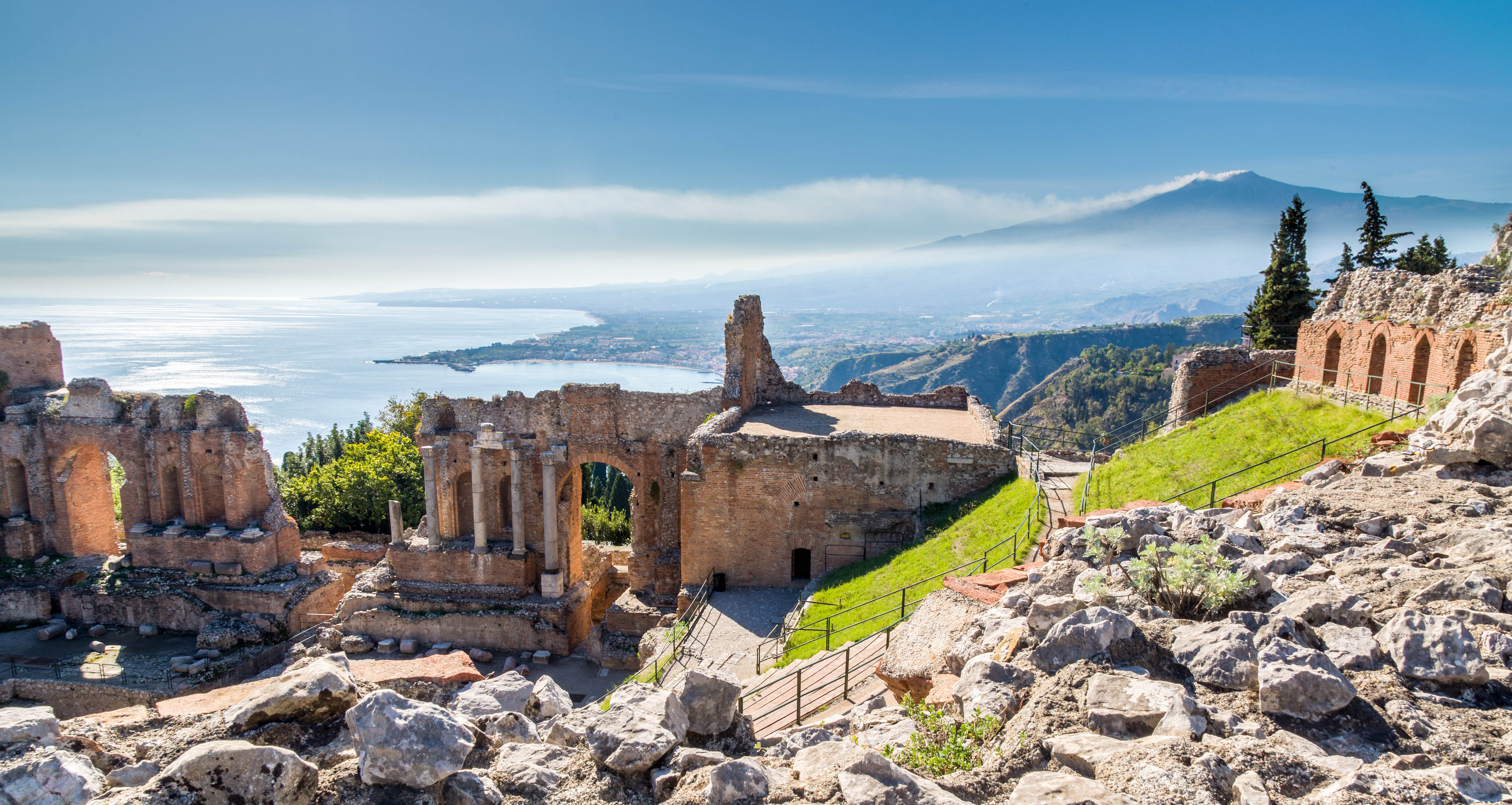 Majestætiske ruiner fra det antikke græske teater i Taormina med den imponerende Etna-vulkan og det glimtende Ioniske Hav i baggrunden på Sicilien