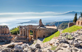 Majestætiske ruiner fra det antikke græske teater i Taormina med den imponerende Etna-vulkan og det glimtende Ioniske Hav i baggrunden på Sicilien