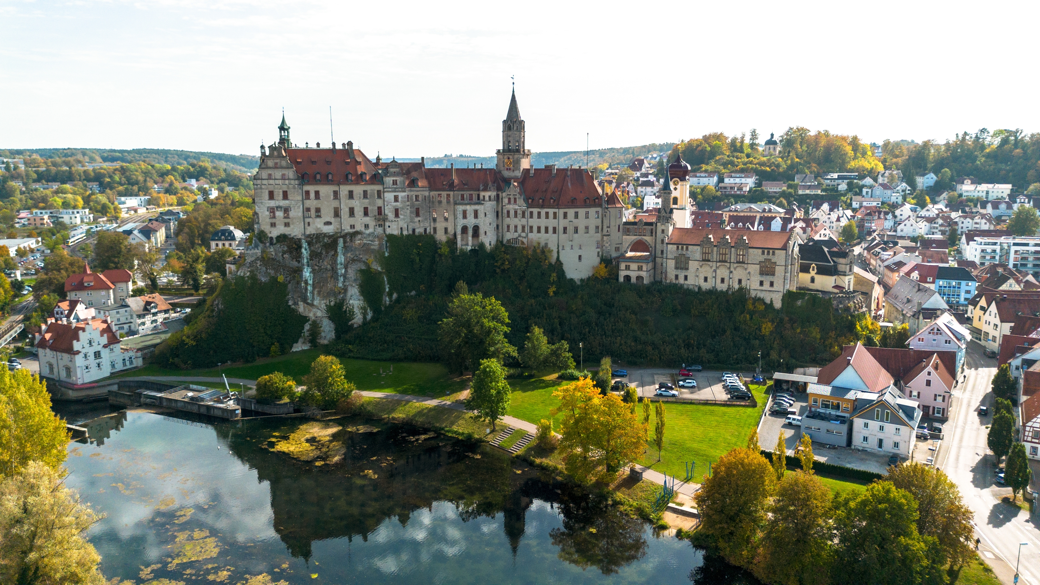 Smukt luftfoto af Sigmaringen Slot placeret dramatisk på en klippe over Donau med farverige efterårstræer og den historiske tyske by i baggrunden