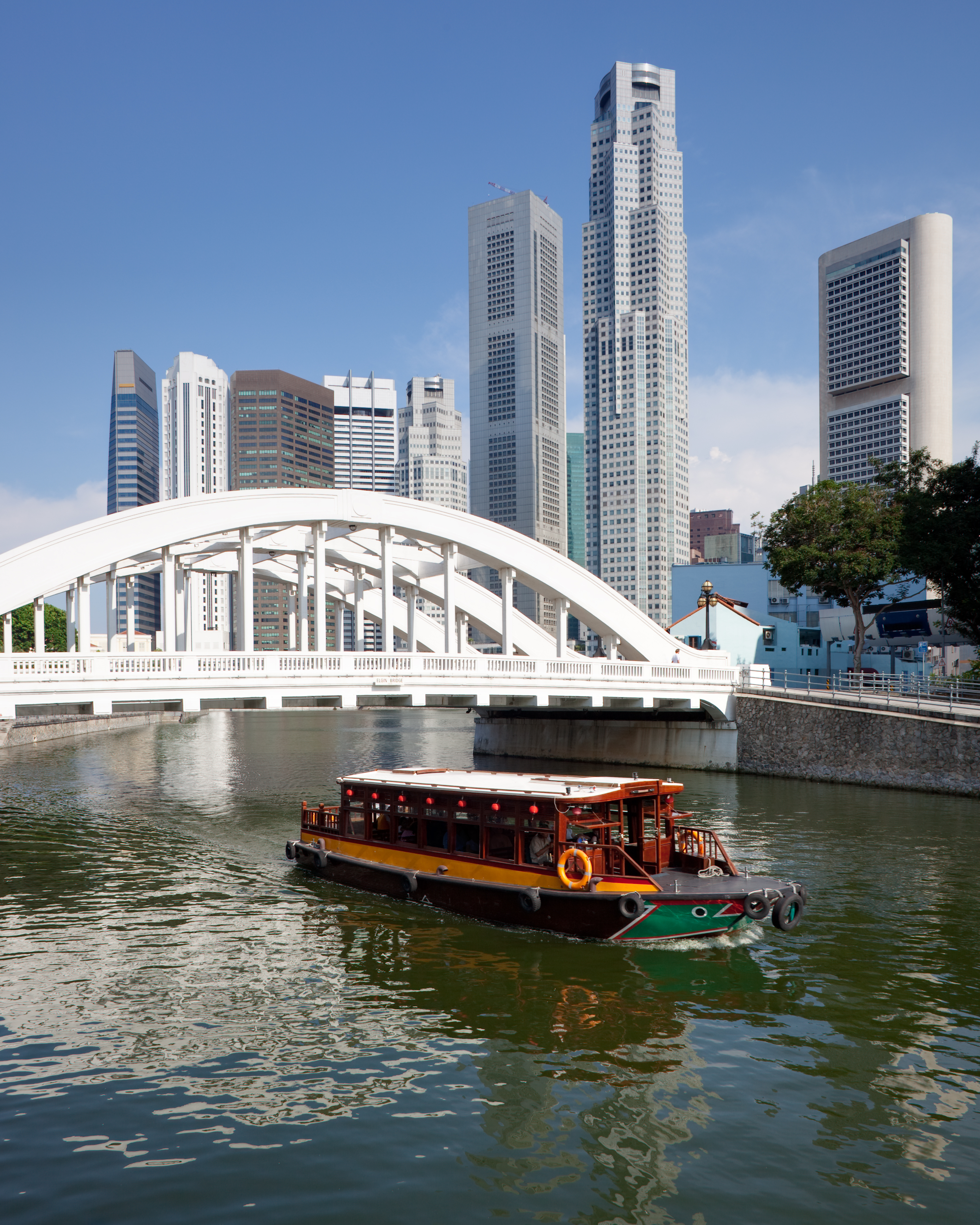 Farverig turistbåd sejler under den hvide Elgin Bridge med Singapores finansdistrikt i baggrunden